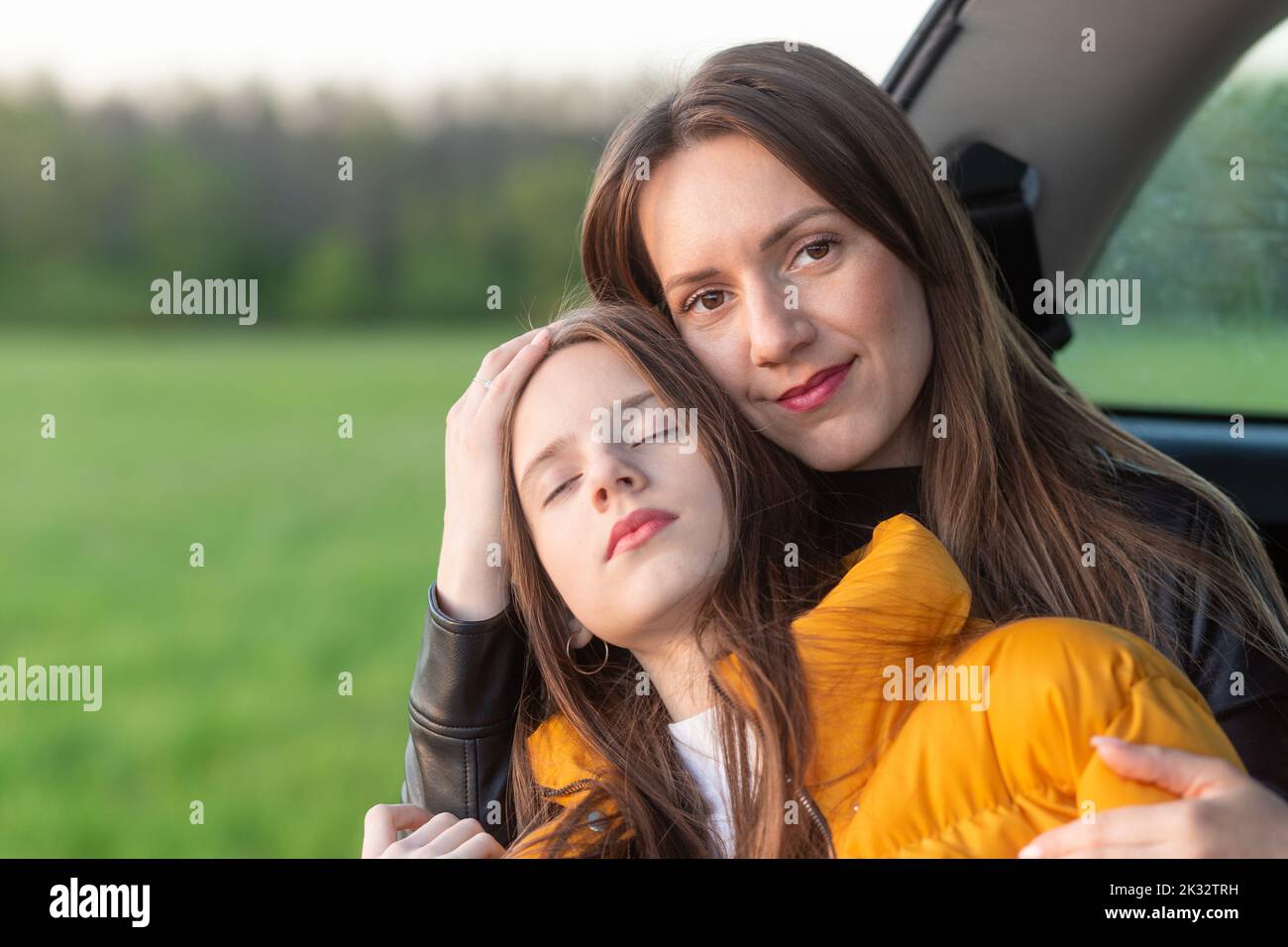 Mother and daughter camping on a hill and admiring the sunset while sitting in the car trunk Stock Photo