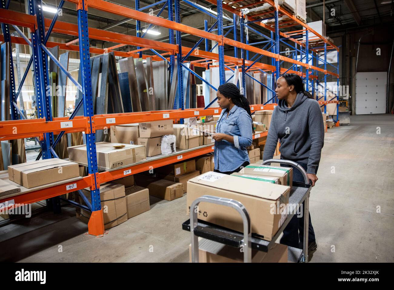 Workers moving boxes with trolley in distribution warehouse Stock Photo