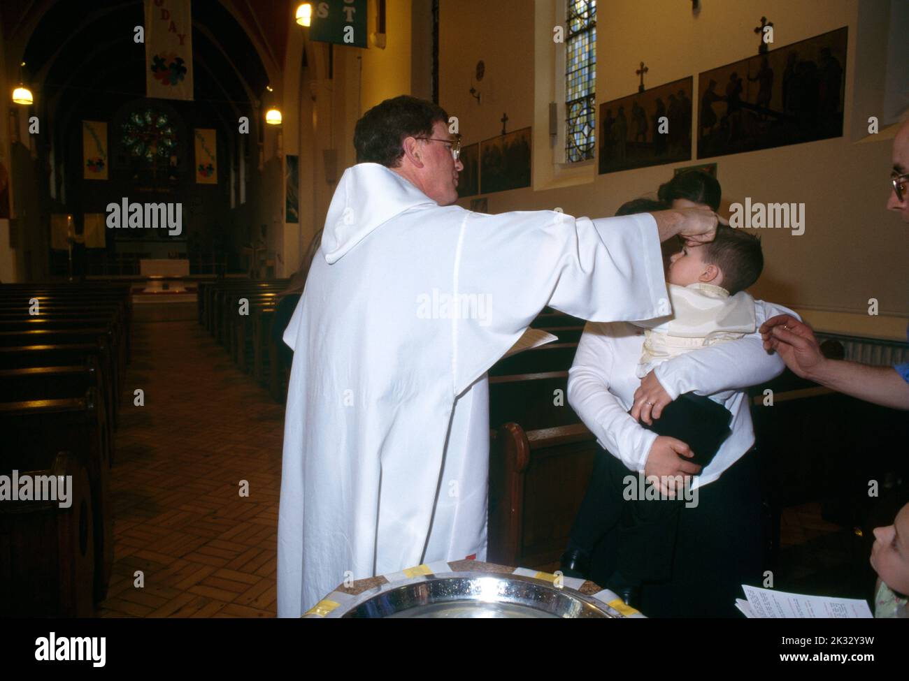 St Joseph's Church Roehampton Priest Anointing Baby With Oil Of Chrism At Font Parents & Godparents Stock Photo