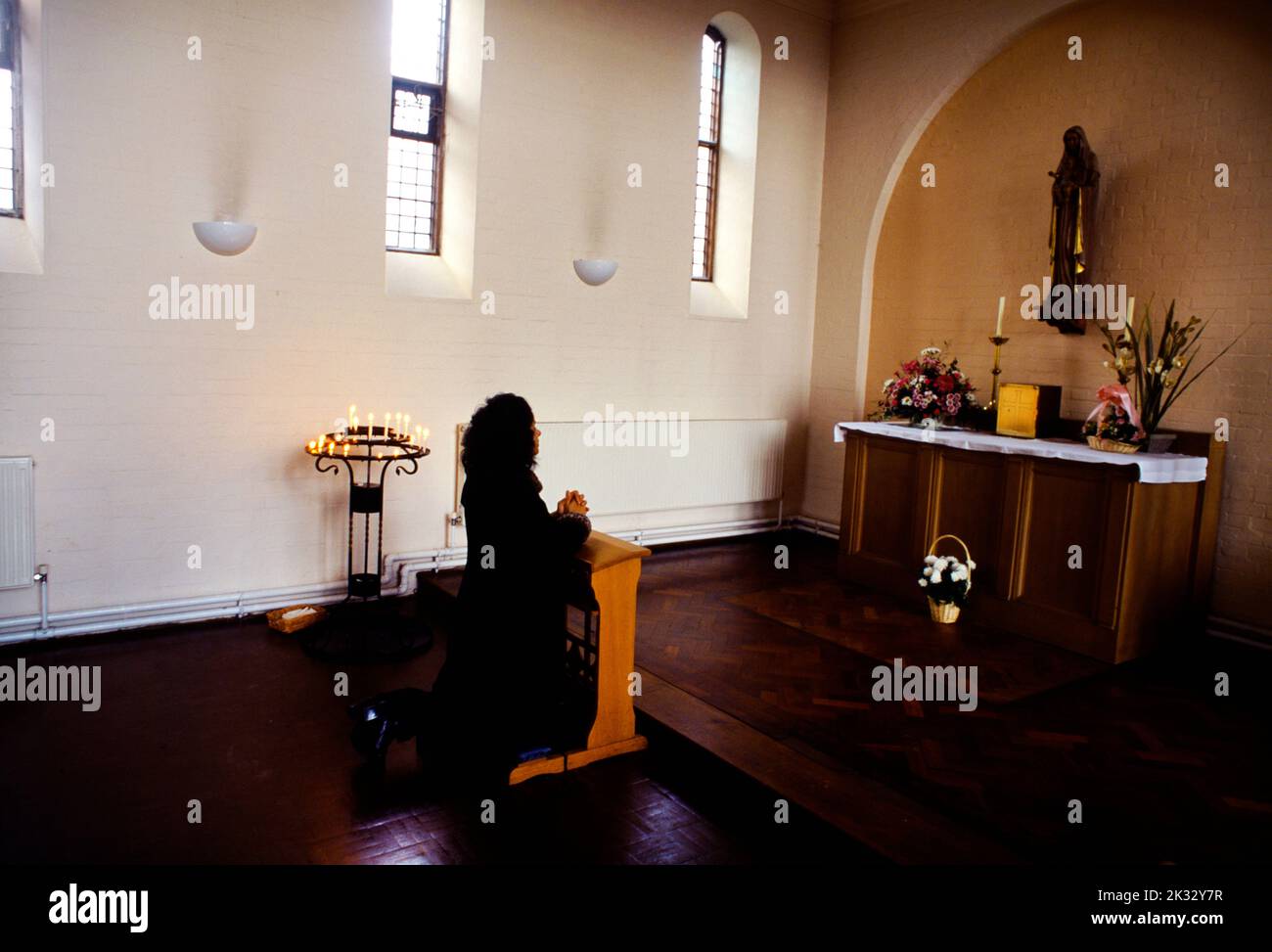 St Cecilias Roman Catholic Cheam Woman Praying Alone In Church looking at Altar with Virgin Mary And Candles Stock Photo