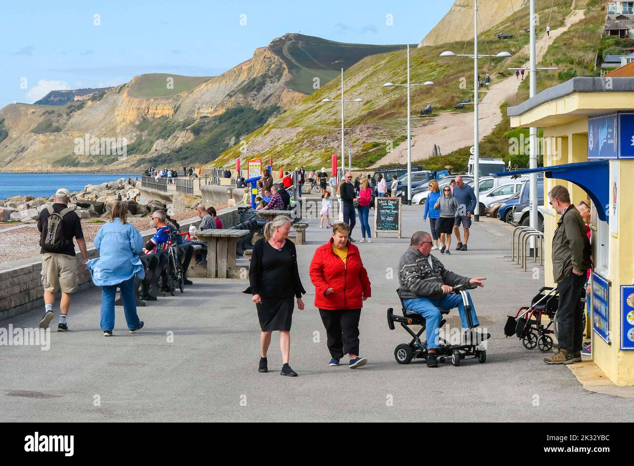West Bay, Dorset, UK.  24th September 2022.  UK Weather.  The seafront at the seaside resort of West Bay in Dorset is busy with visitors and locals enjoying the warm afternoon hazy autumn sunshine.  Picture Credit: Graham Hunt/Alamy Live News Stock Photo