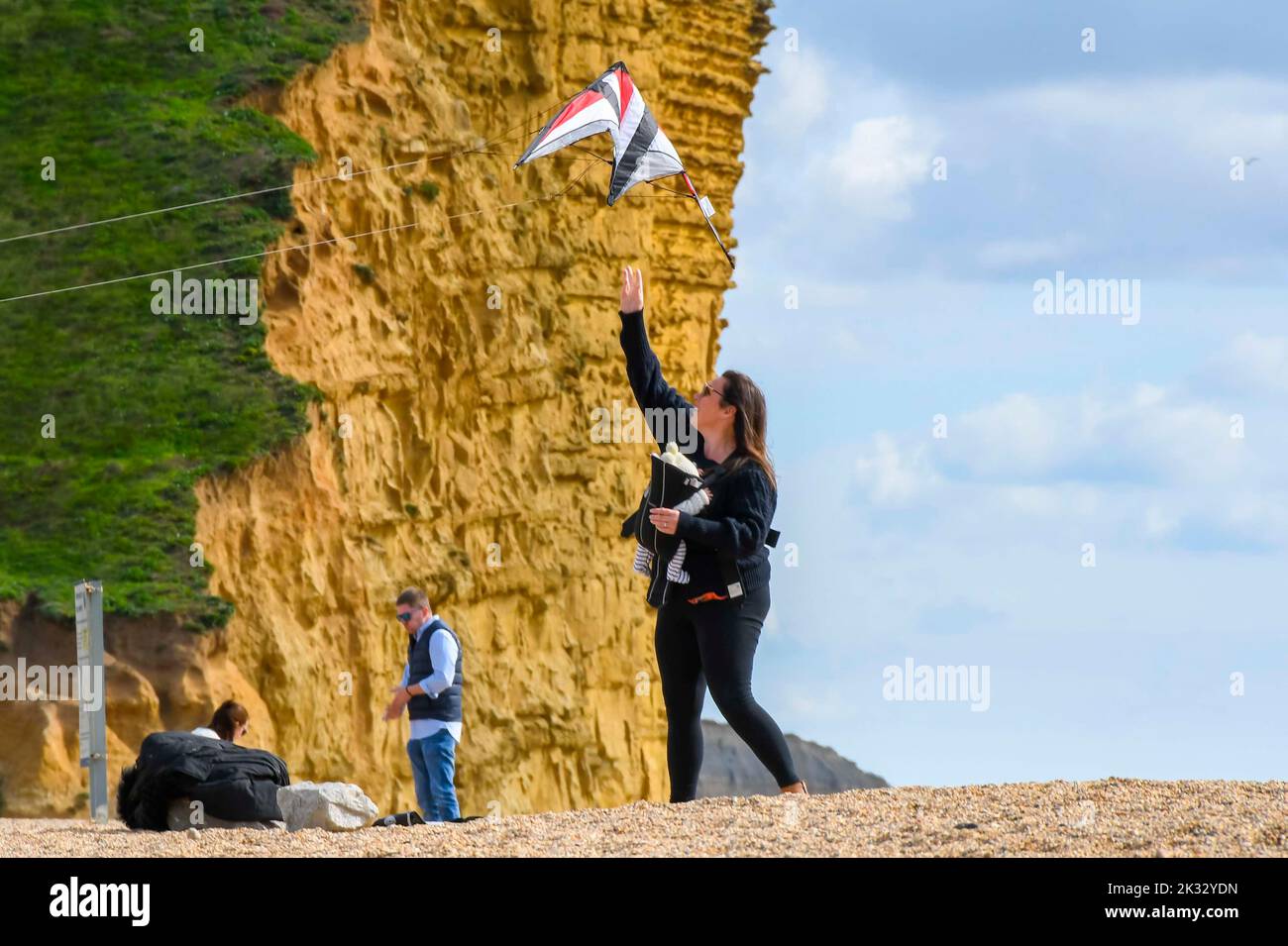 West Bay, Dorset, UK.  24th September 2022.  UK Weather.  A woman launches a kite from the beach at the seaside resort of West Bay in Dorset on a warm afternoon with hazy autumn sunshine.  Picture Credit: Graham Hunt/Alamy Live News Stock Photo