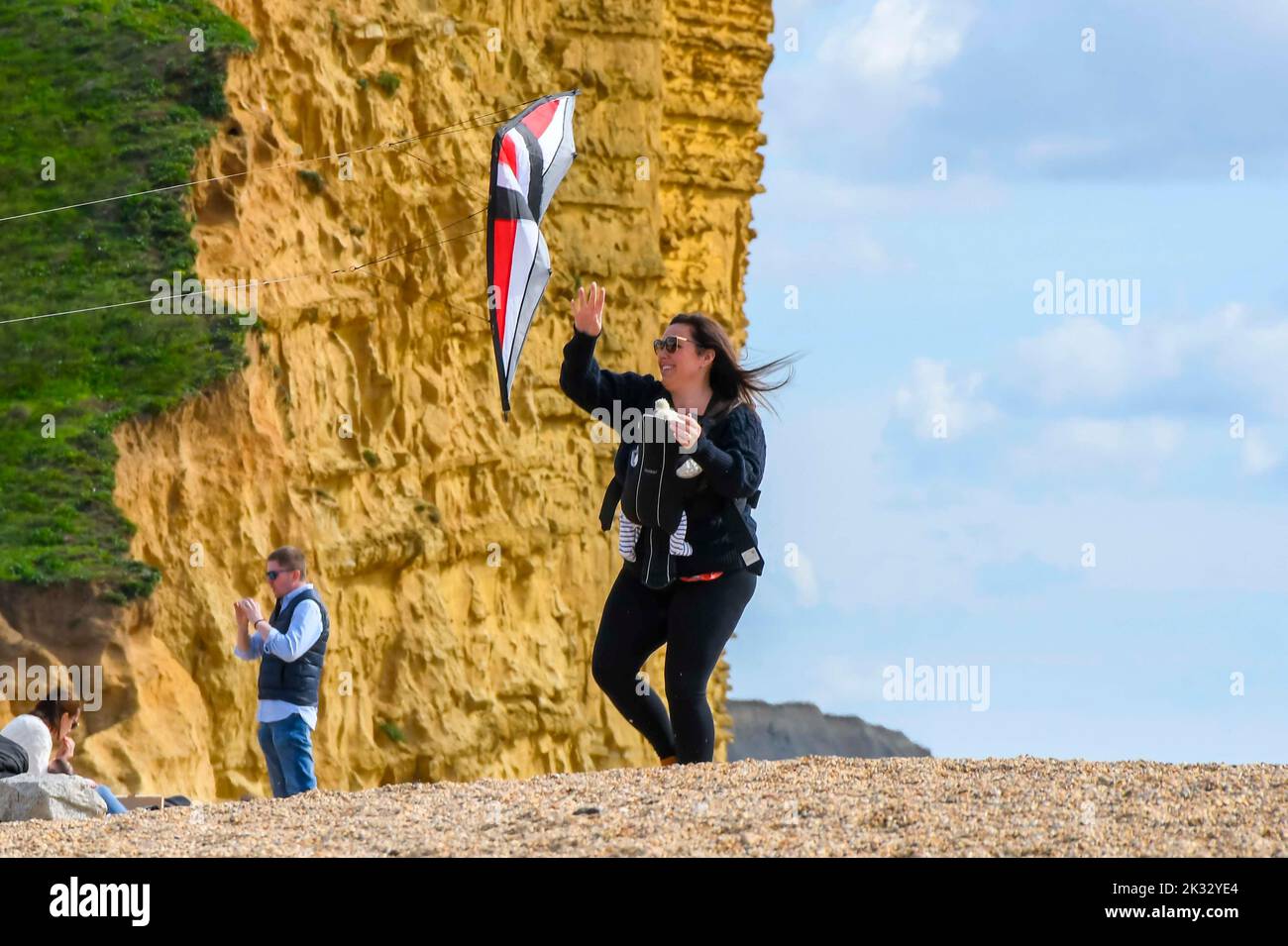 West Bay, Dorset, UK.  24th September 2022.  UK Weather.  A woman launches a kite from the beach at the seaside resort of West Bay in Dorset on a warm afternoon with hazy autumn sunshine.  Picture Credit: Graham Hunt/Alamy Live News Stock Photo