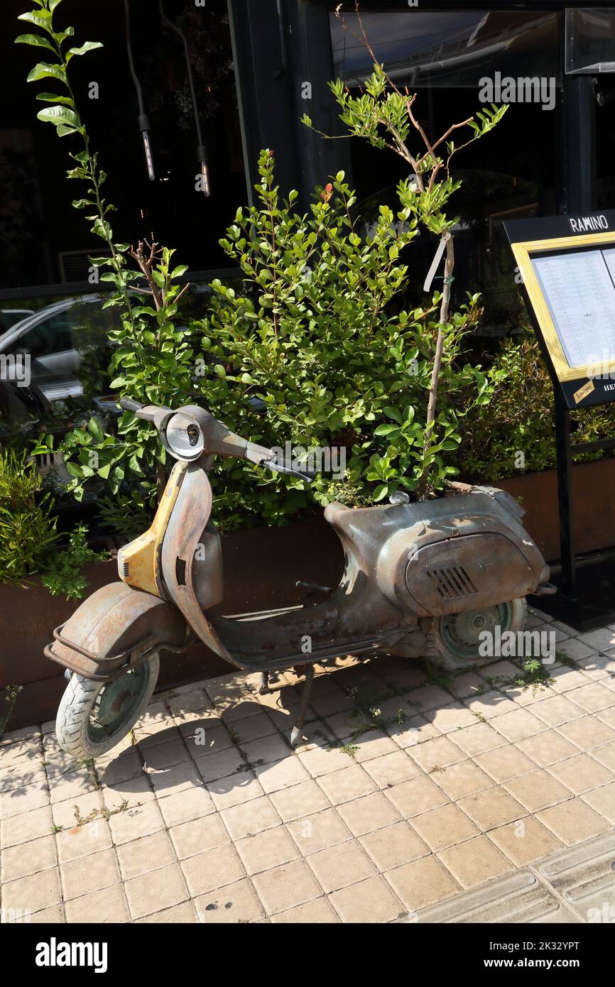 Old Vespa Scooter that has been reused as a Plant holder With Tree Where Engine used to Be outside restaurant Glyfada Athens Greece Stock Photo