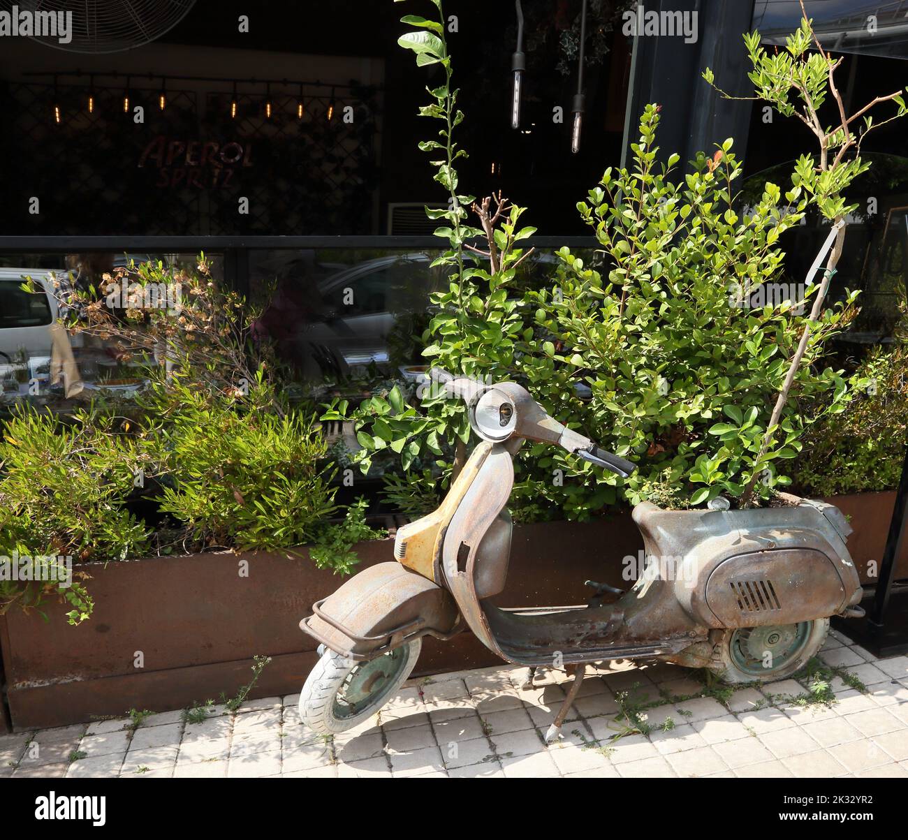 Old Vespa Scooter that has been reused as a Plant holder With Tree Where Engine used to Be outside restaurant Glyfada Athens Greece Stock Photo