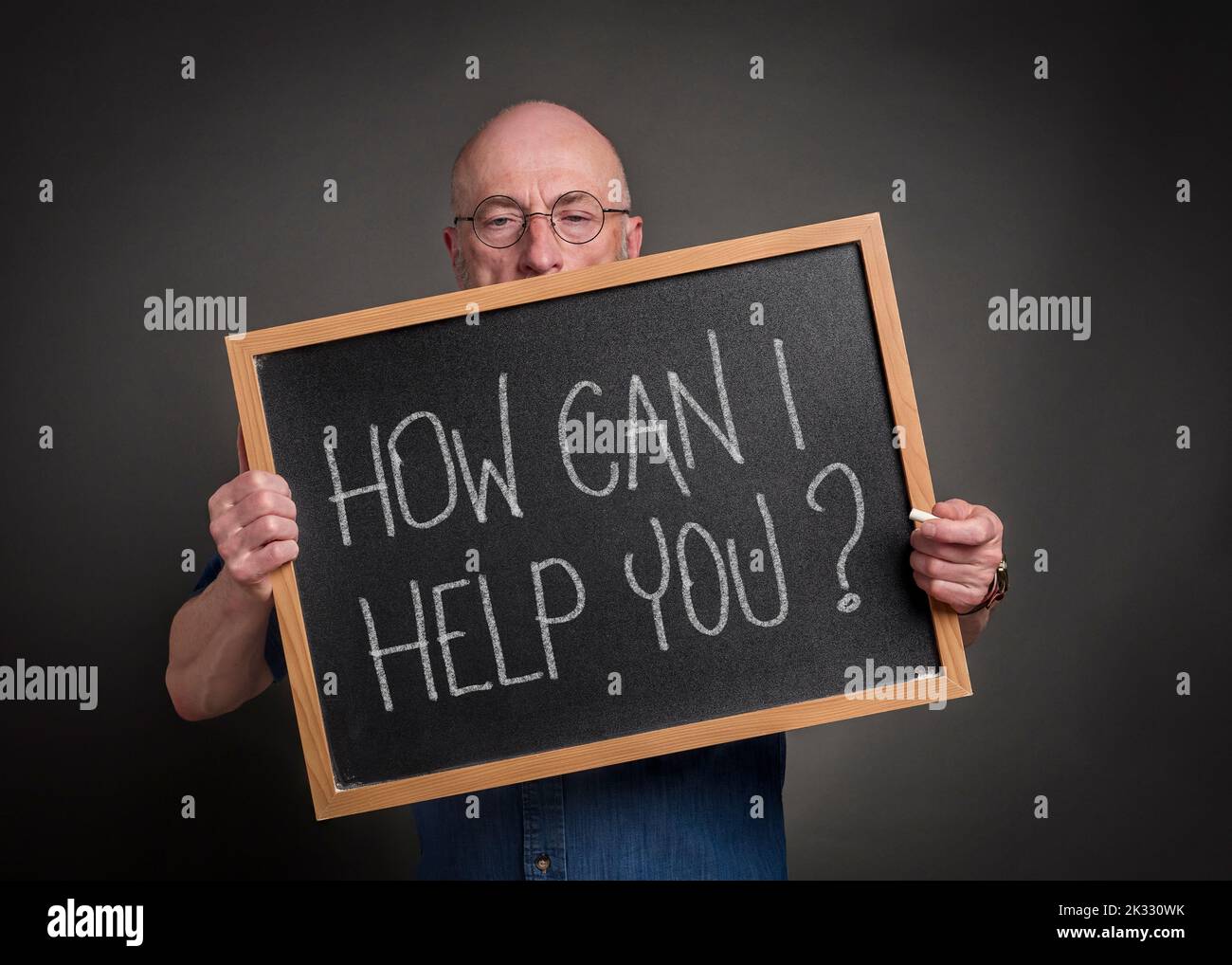 How can I help you? Senior man, teacher, mentor or presenter with a blackboard sign, education, presentation and business communication concept. Stock Photo