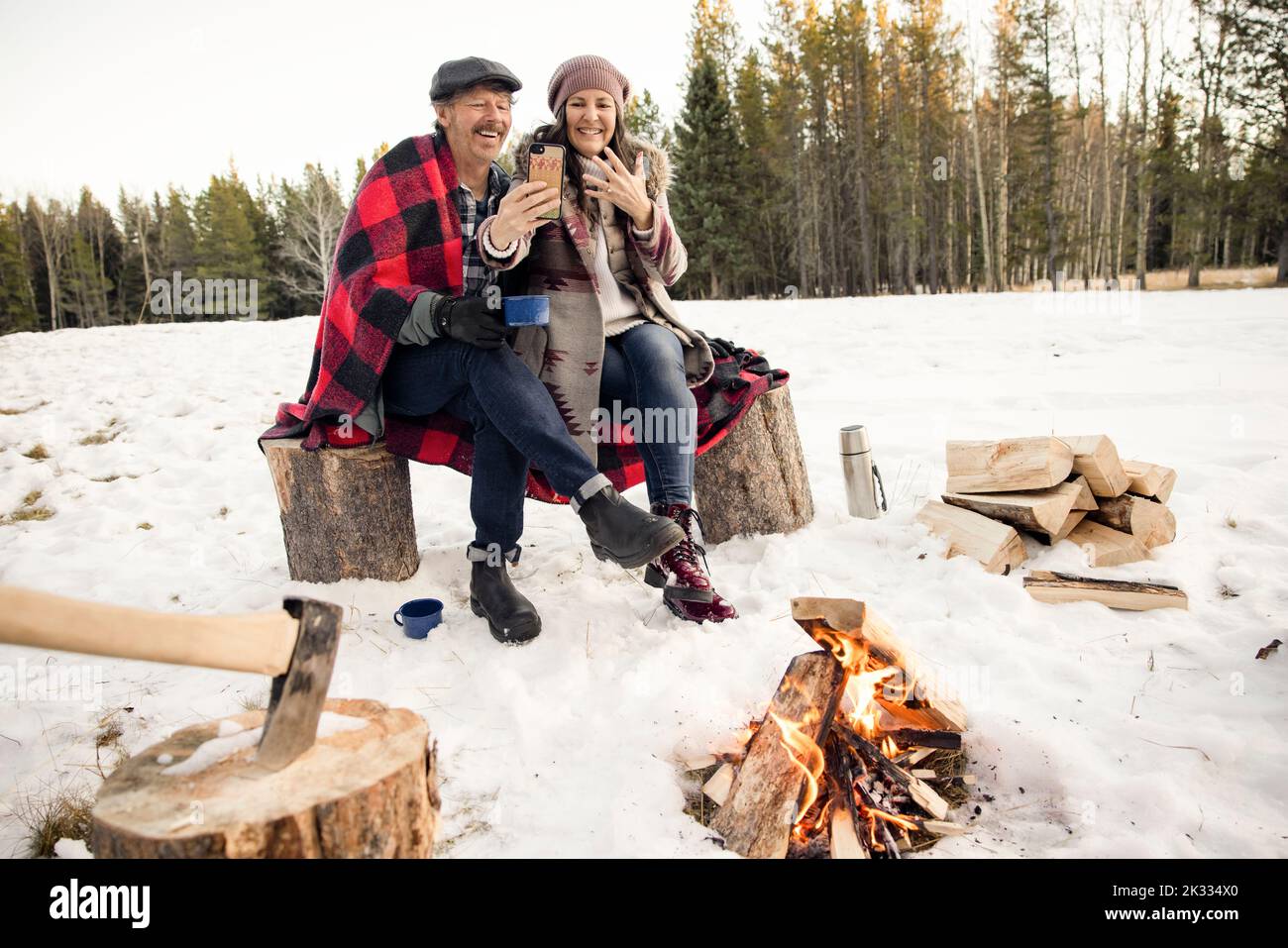 Couple looking at photo on phone next to fire in snow Stock Photo