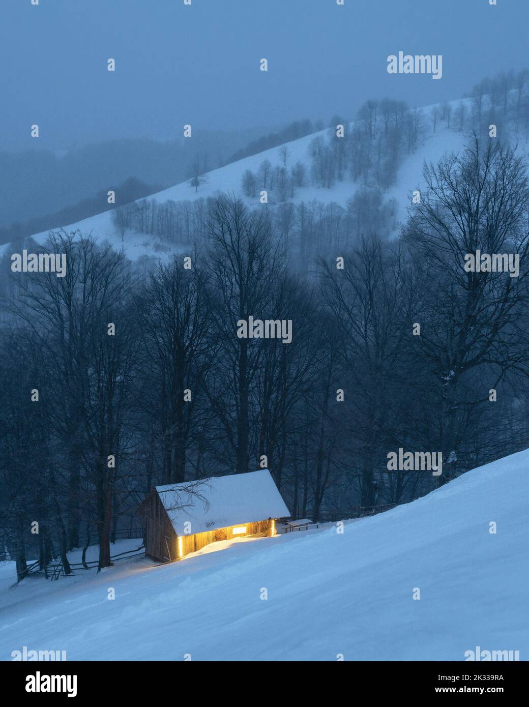 Evening twilight view of a lonely cabin in a snowy mountain forest in winter Stock Photo