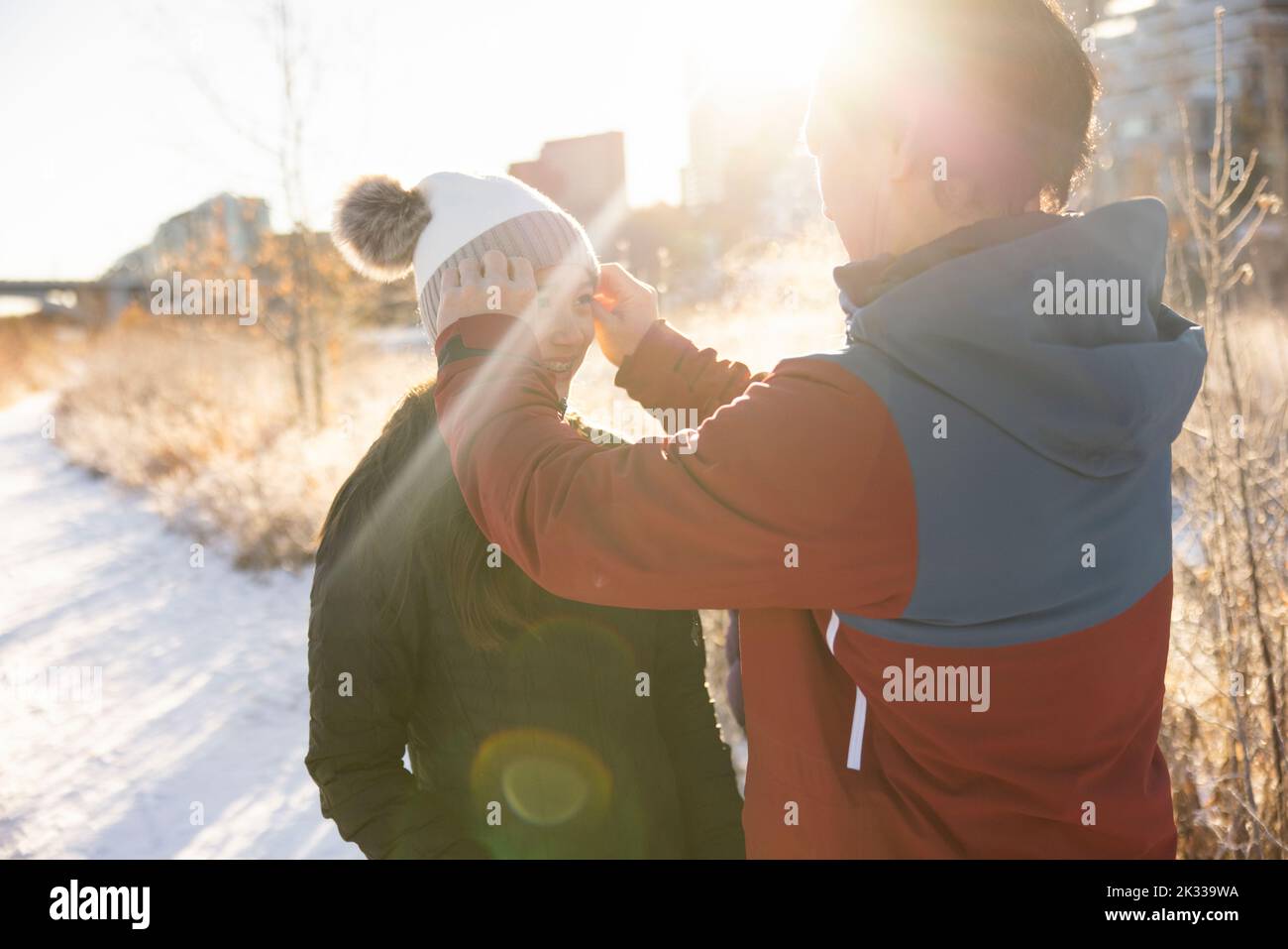 Father adjusting stocking cap on teen daughter in sunny snowy park Stock Photo