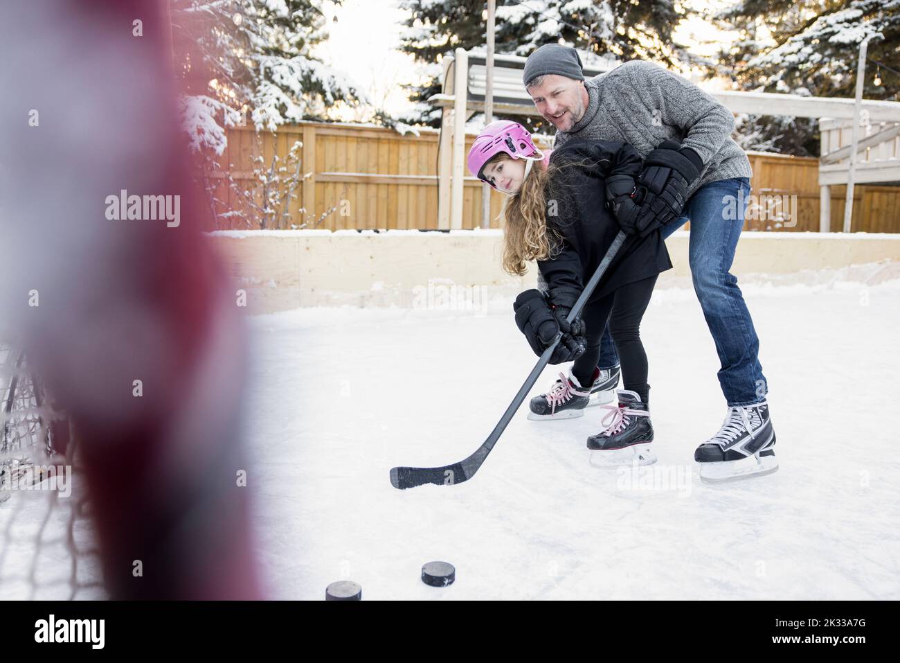 Father teaching daughter to play ice hockey on backyard ice rink Stock