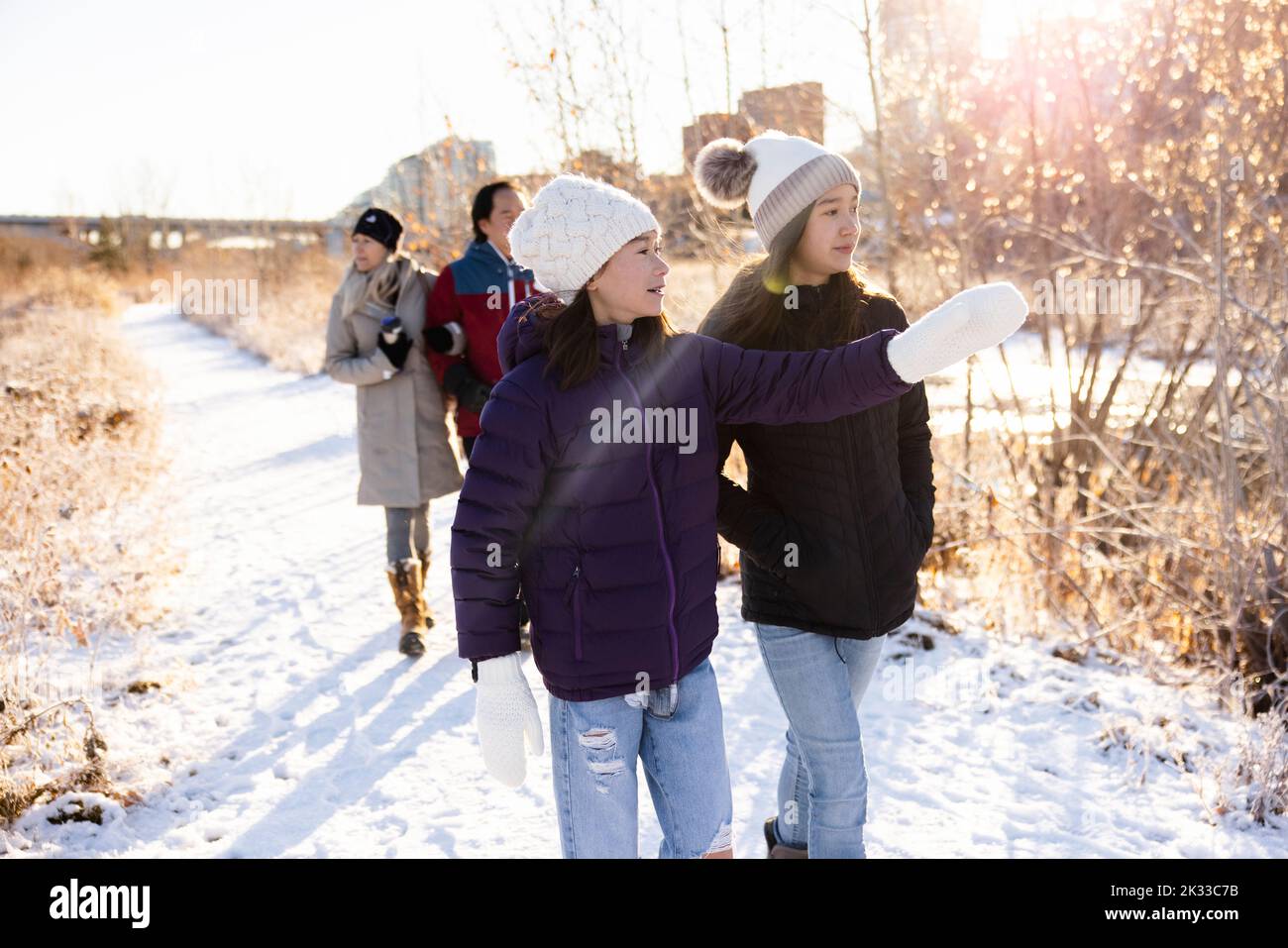 Teenage sisters walking on path in sunny snowy winter city park Stock Photo
