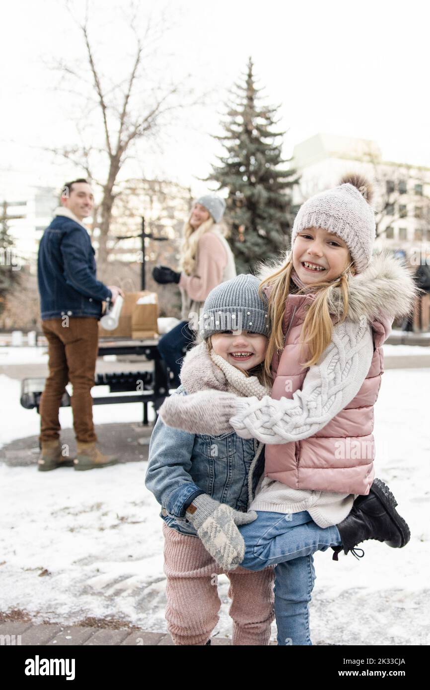 Portrait playful cute sisters in knit hats in snowy winter city park Stock Photo