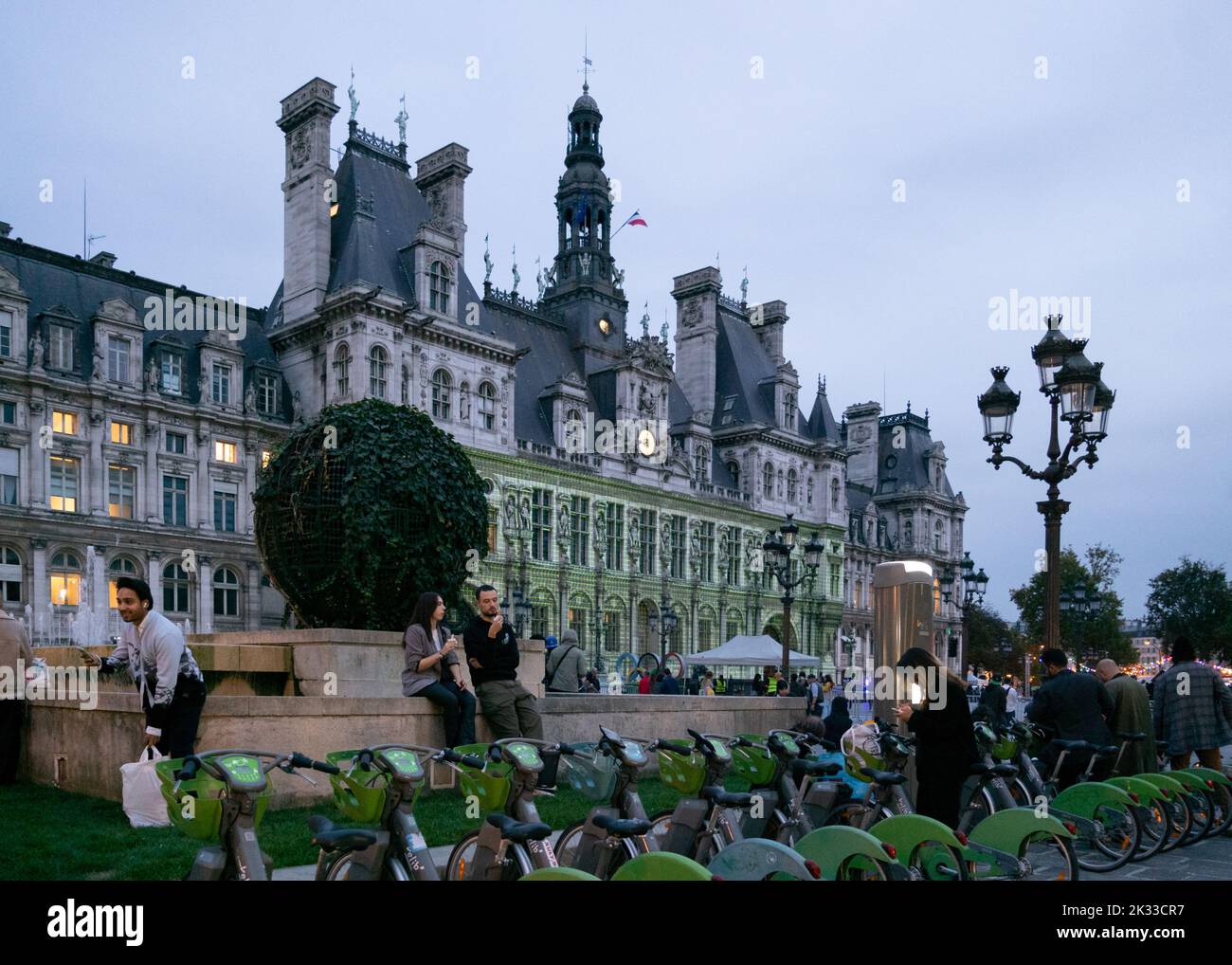 The green Vélib' are neatly parked by the City Hall of Paris where a light show is projected on its facade Stock Photo