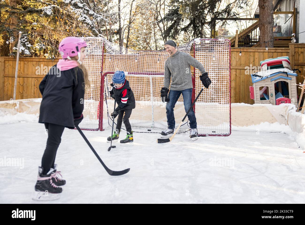 Father and kids playing hockey on backyard ice rink Stock Photo Alamy