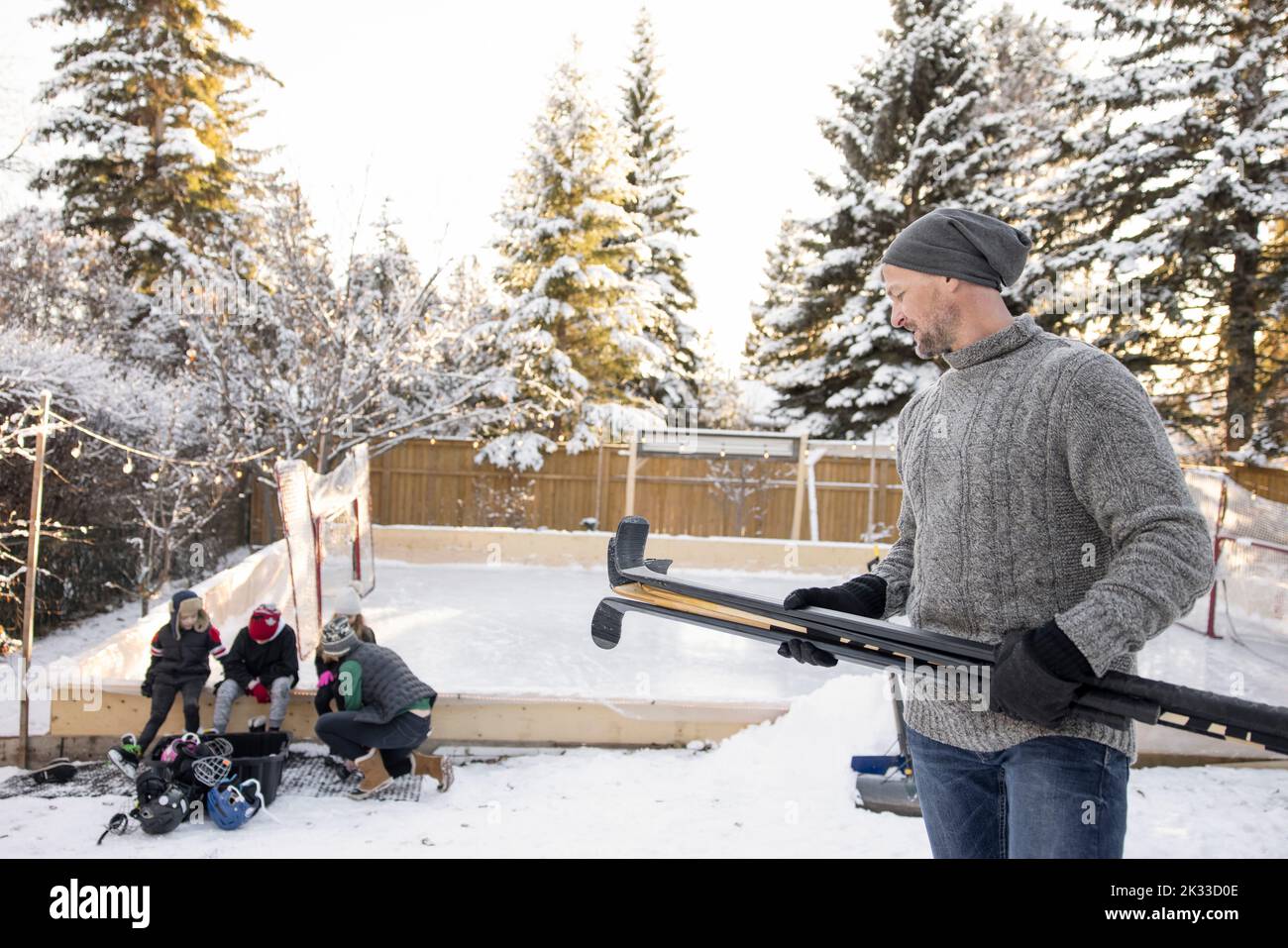 Family with ice hockey equipment at snowy backyard ice rink Stock Photo