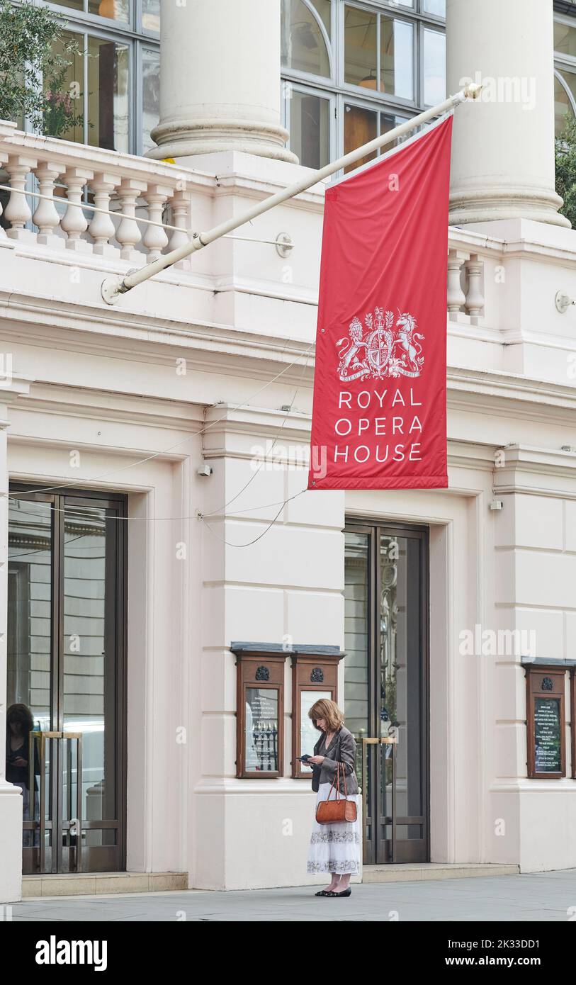 A woman on her phone outside the main entrance to the Royal Opera House (roh), Bow Street, London, England Stock Photo