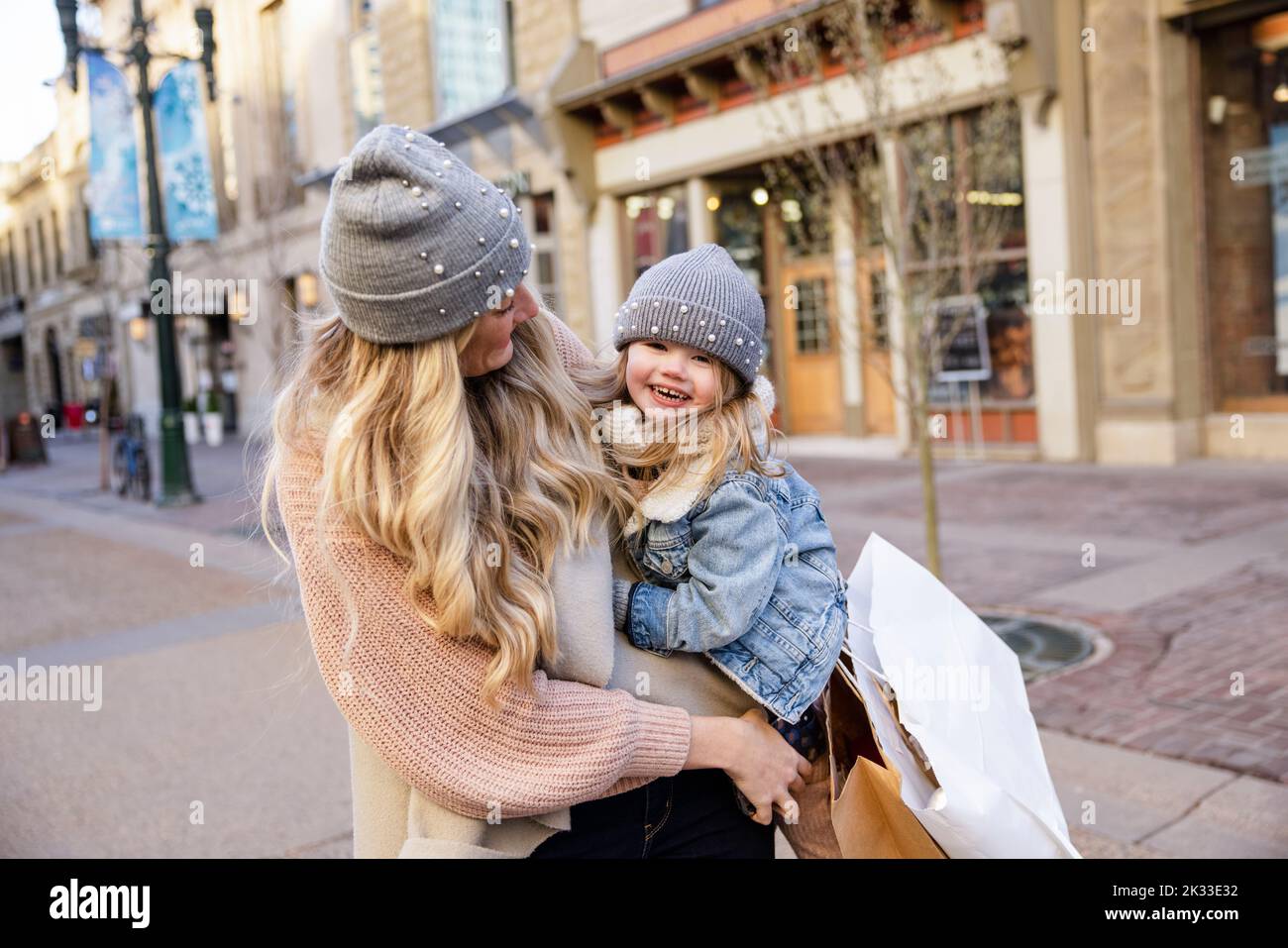 Portrait happy blonde mother and daughter in knit hats on city street Stock Photo