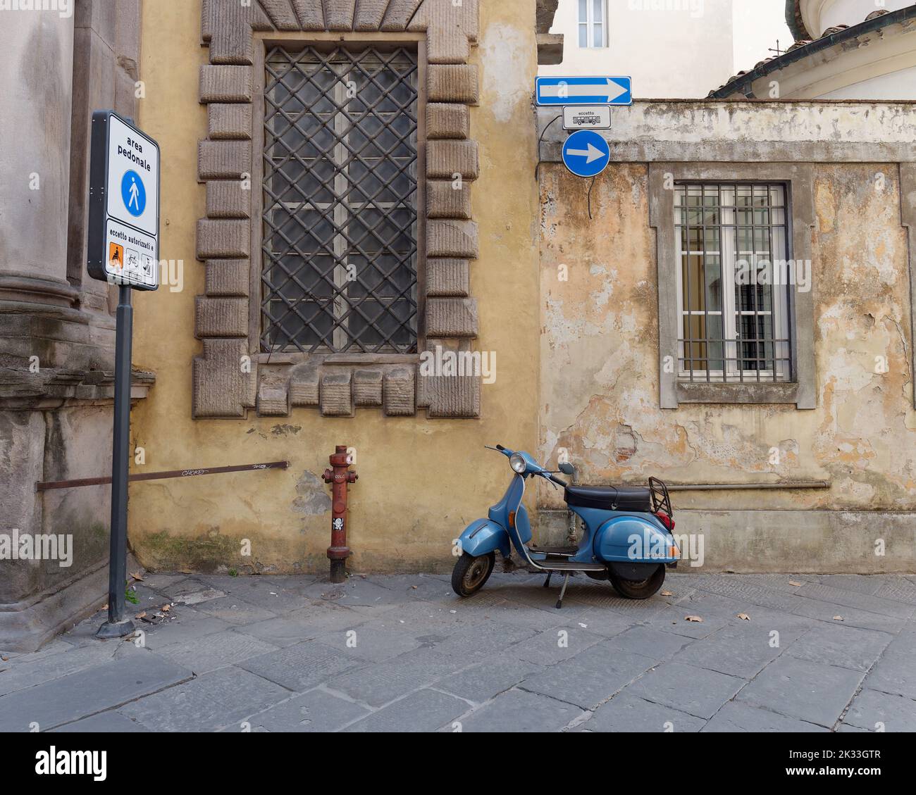 Blue Vespa and a yellow building wiith large windows on a one way street in the town of Lucca, Tuscany, Italy Stock Photo