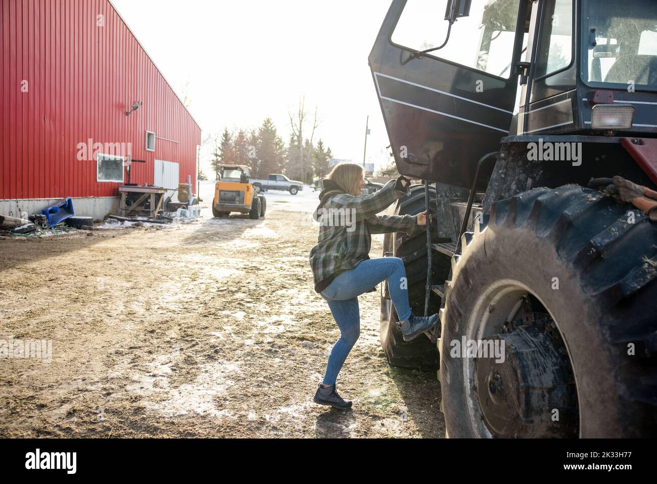 Girl climbing into tractor on farmyard Stock Photo