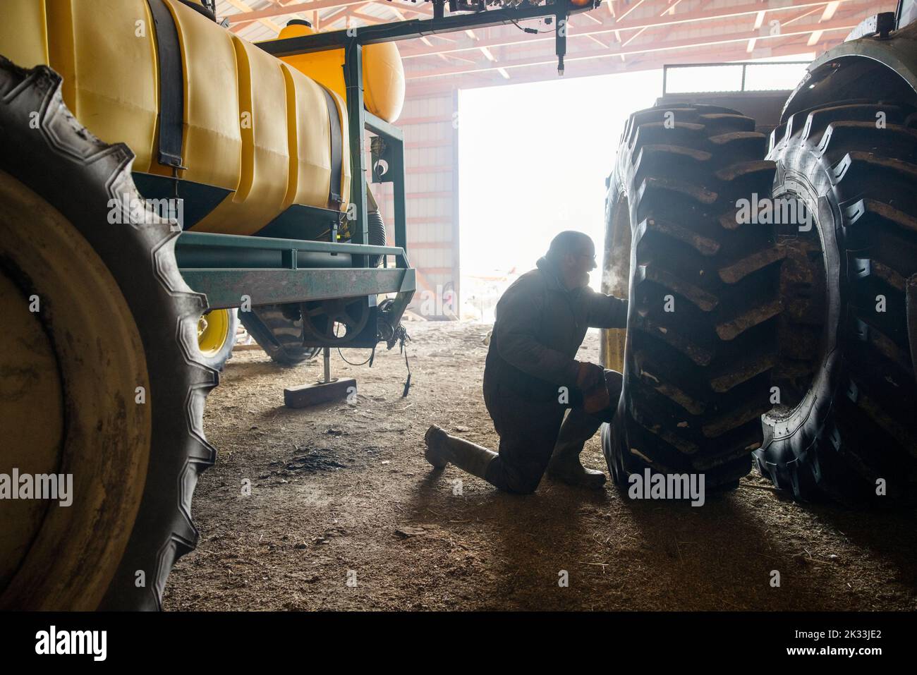 Farmer fixing tire of tractor in barn Stock Photo