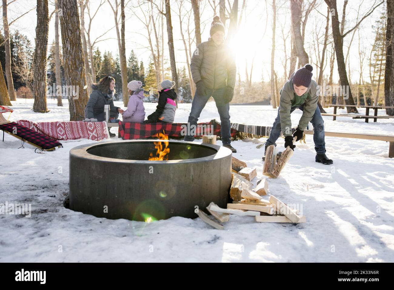 Grandfather watching grandson chop firewood at campfire in snowy woods