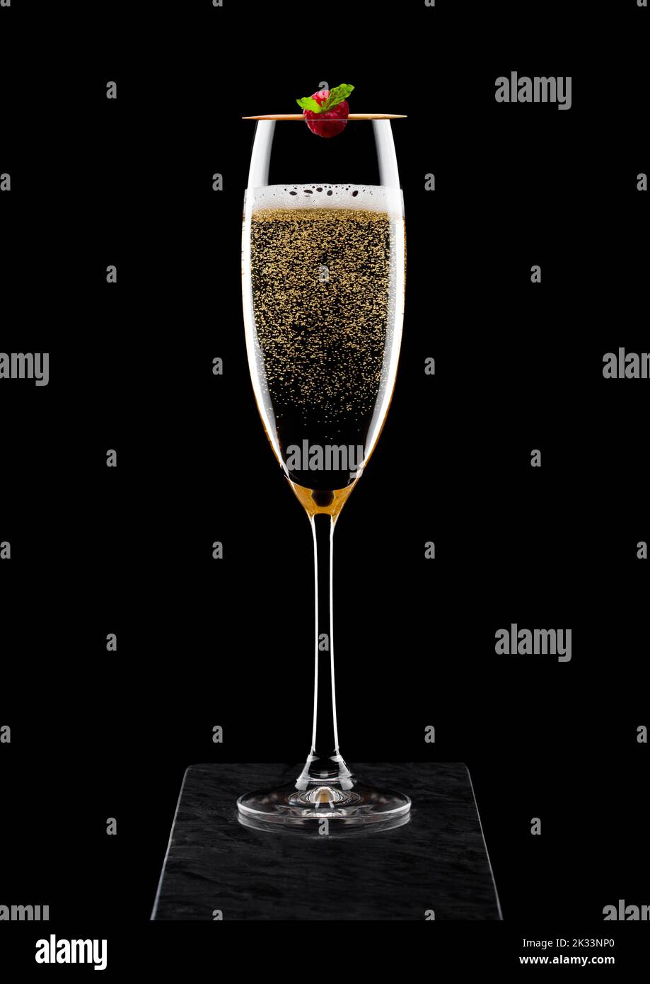 Elegant glass of yellow champagne with rasspbery on stick on black marble board on black Stock Photo