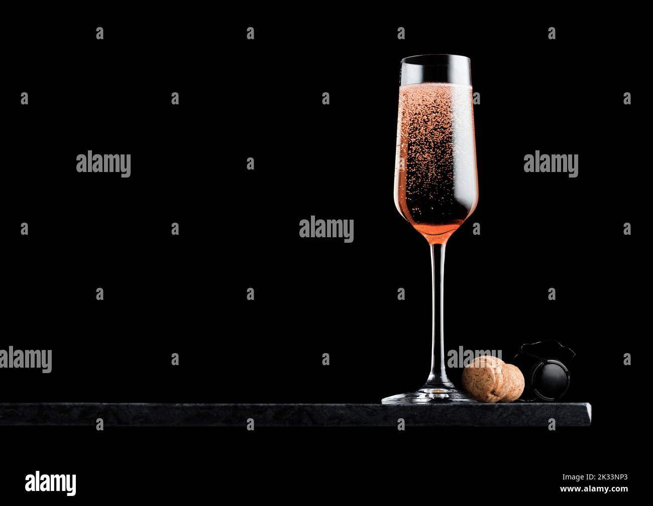 Elegant glass of pink rose champagne with cork and wire cage on black marble board on black background. Stock Photo