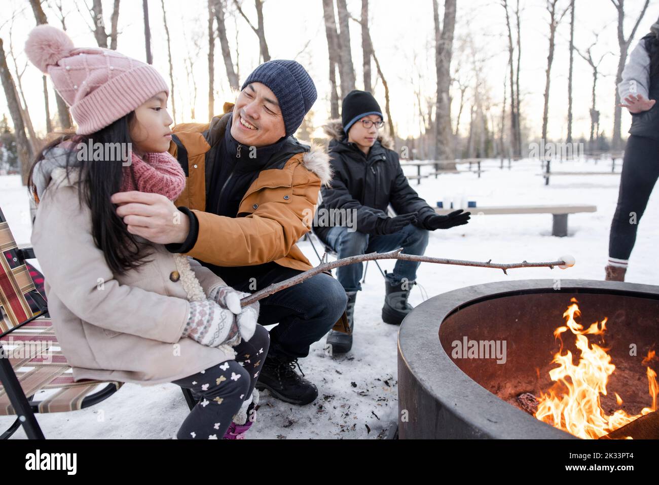 Happy family roasting marshmallows at fire pit in snowy winter park Stock Photo