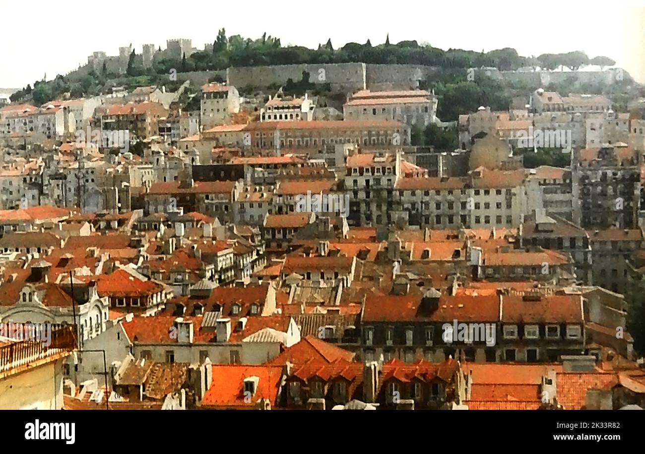 A vintage view (1970s) over the rooftops of Lisbon, Portugal, looking towards the walls of the citadel and São Jorge Castle. The Citadel of Cascais is a group of 15th to 17th century defences  for Portugal's  Capital city , Lisbon., its coastline and the River Tagus. The tower of Santo António de Cascais, the Fortress of Our Lady of Light (Nossa Senhora da Luz de Cascais), and the former Royal Palace  are all encompassed within the citadel.. Stock Photo