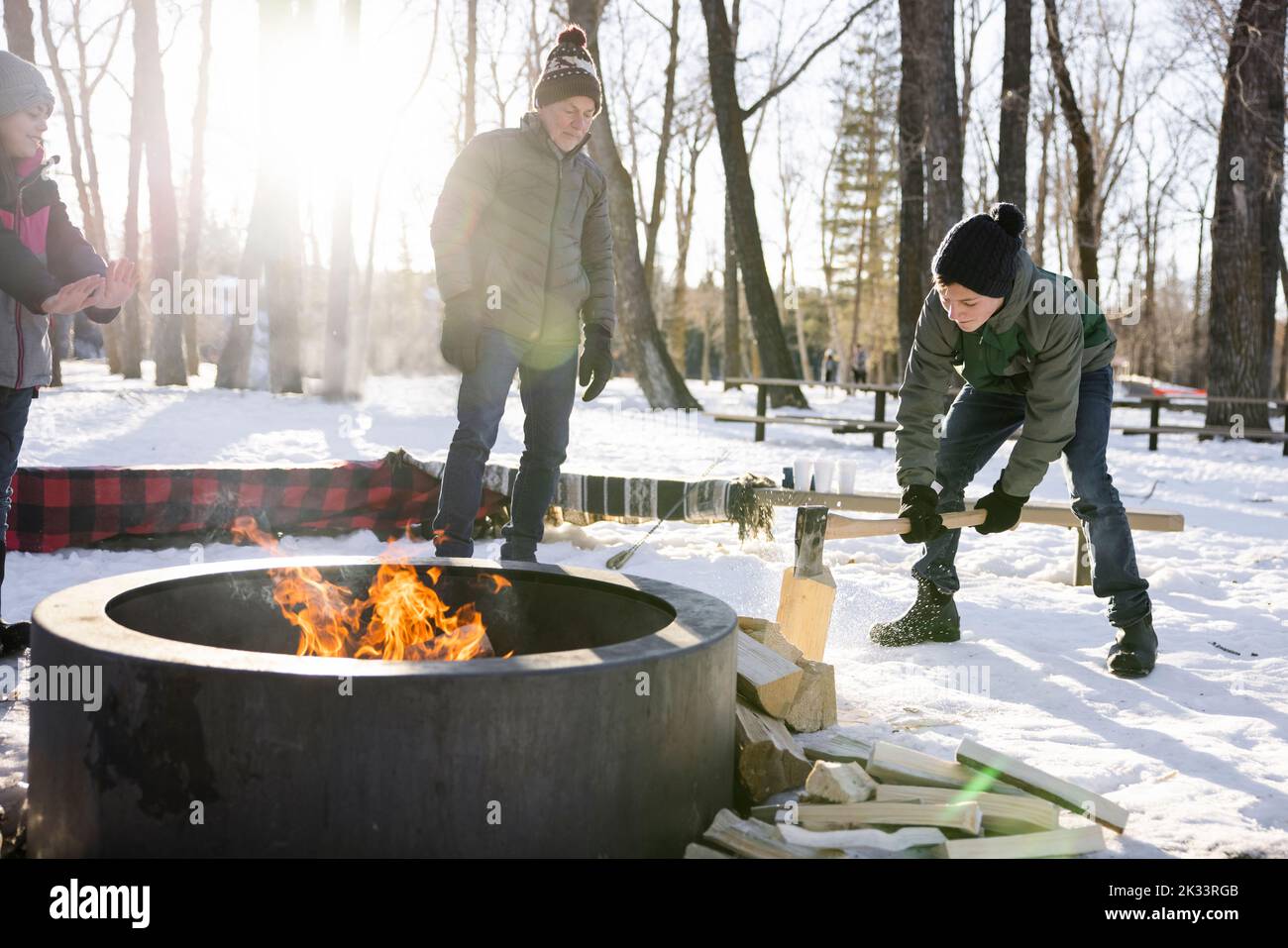 Grandfather watching grandson chop firewood at campfire in winter park