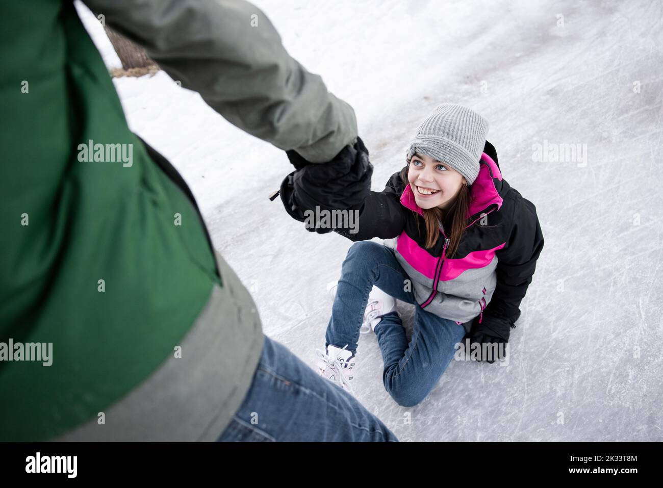 boy-helping-happy-sister-get-up-after-falling-while-ice-skating-stock