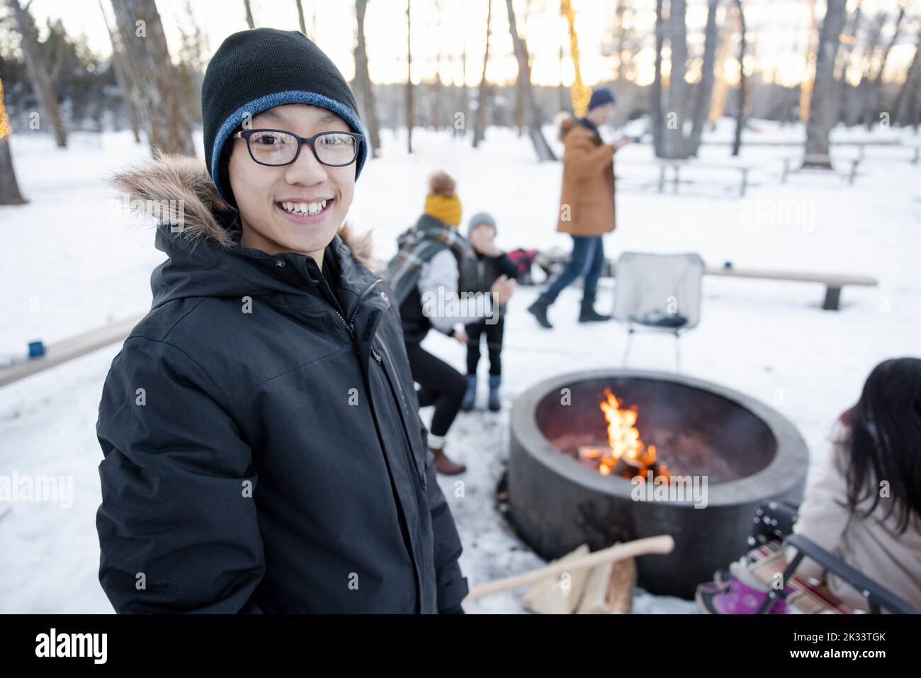 Portrait happy teen boy at fire pit with family in snowy winter park Stock Photo