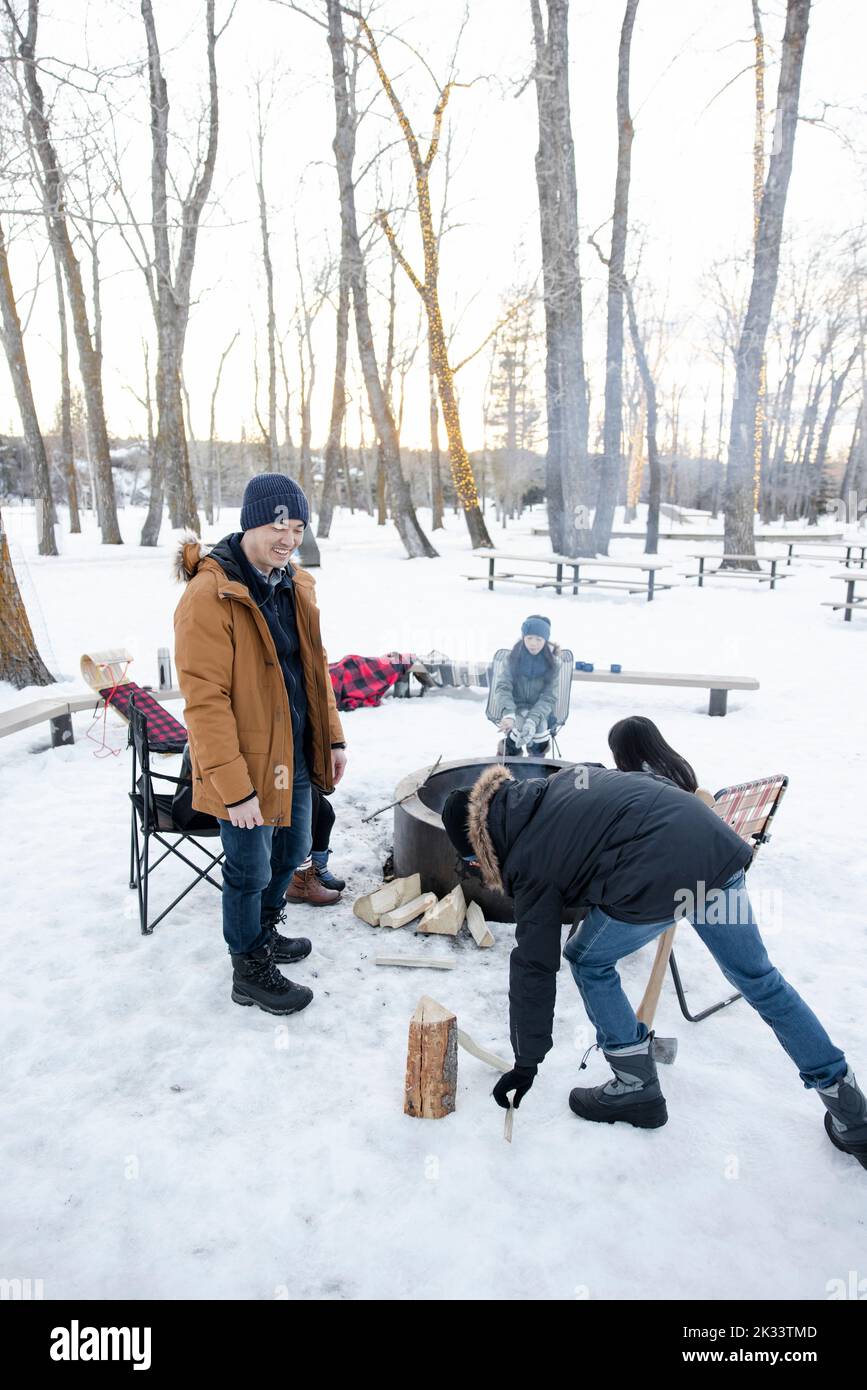 Family chopping firewood at fire pit in snowy winter park Stock Photo