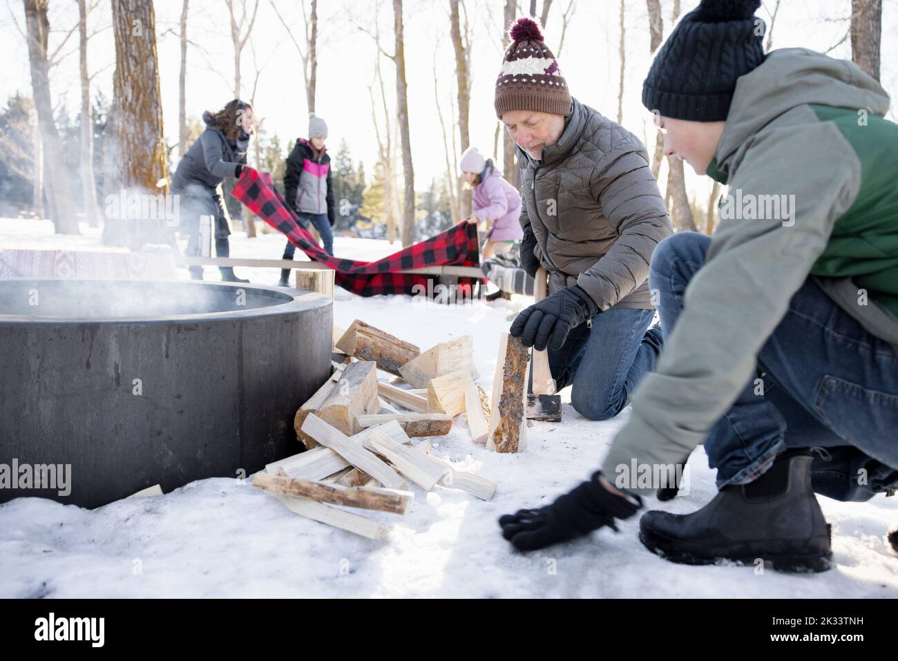 Grandfather and grandson chopping firewood at campfire in snowy woods