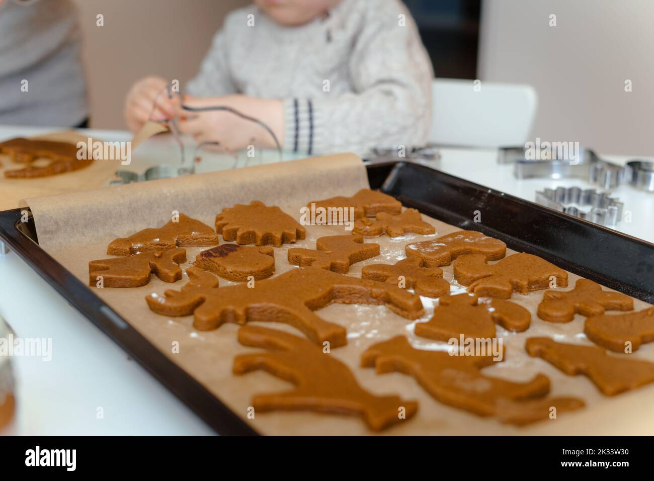 In the foreground are baking trays with Christmas gingerbread in the shape of animals, in the background are the hands of a child Stock Photo