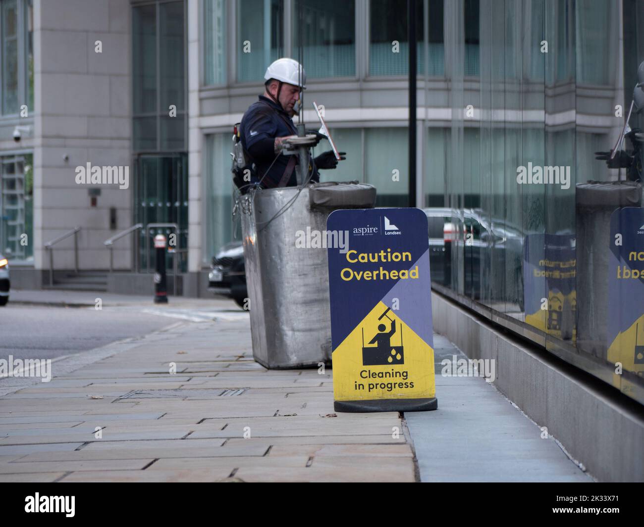 Window cleaners preparing to ascend tall building in cradle with Caution overhead, cleaning in