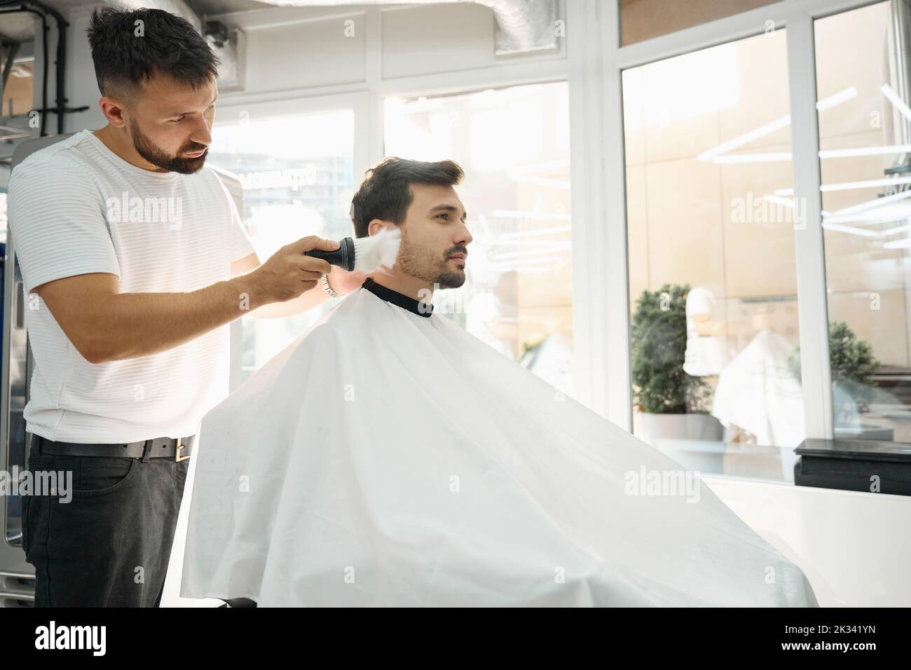 Professional barber sweeping pieces of shaved hair off of client Stock Photo