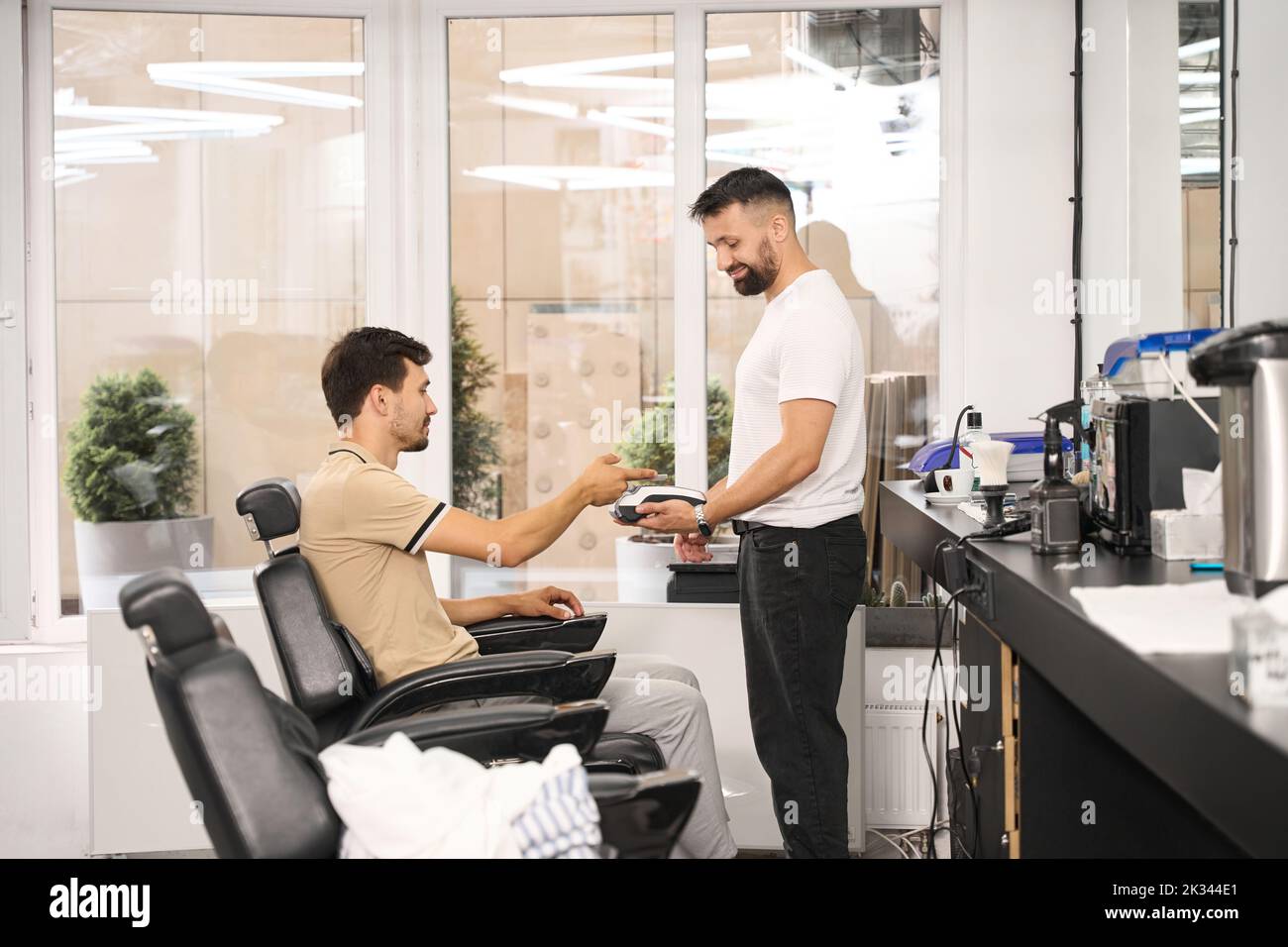 Client of hair salon paying for service cashlessly and contactlessly Stock Photo