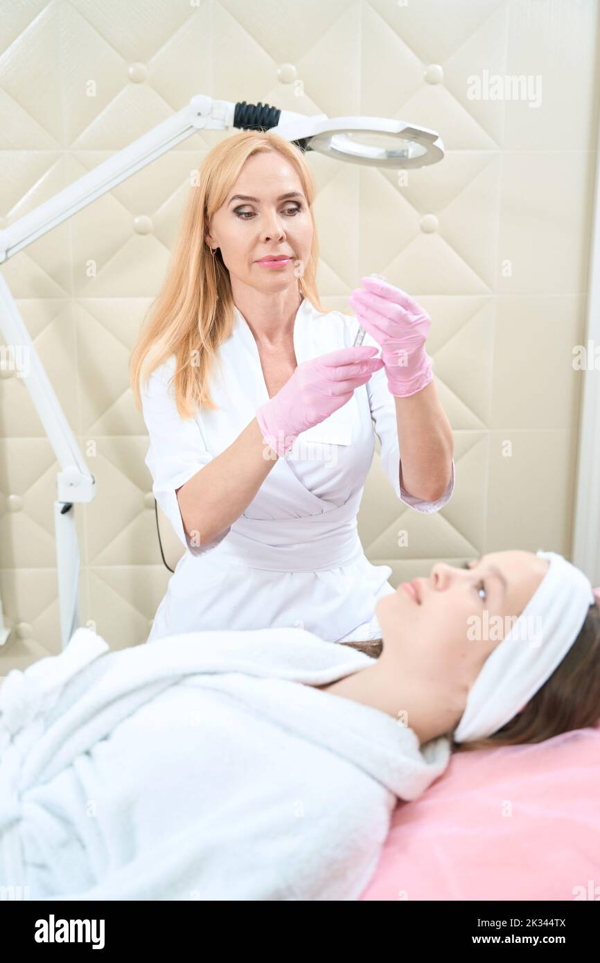 Focused woman beautician is typing injection from jar with syringe Stock Photo