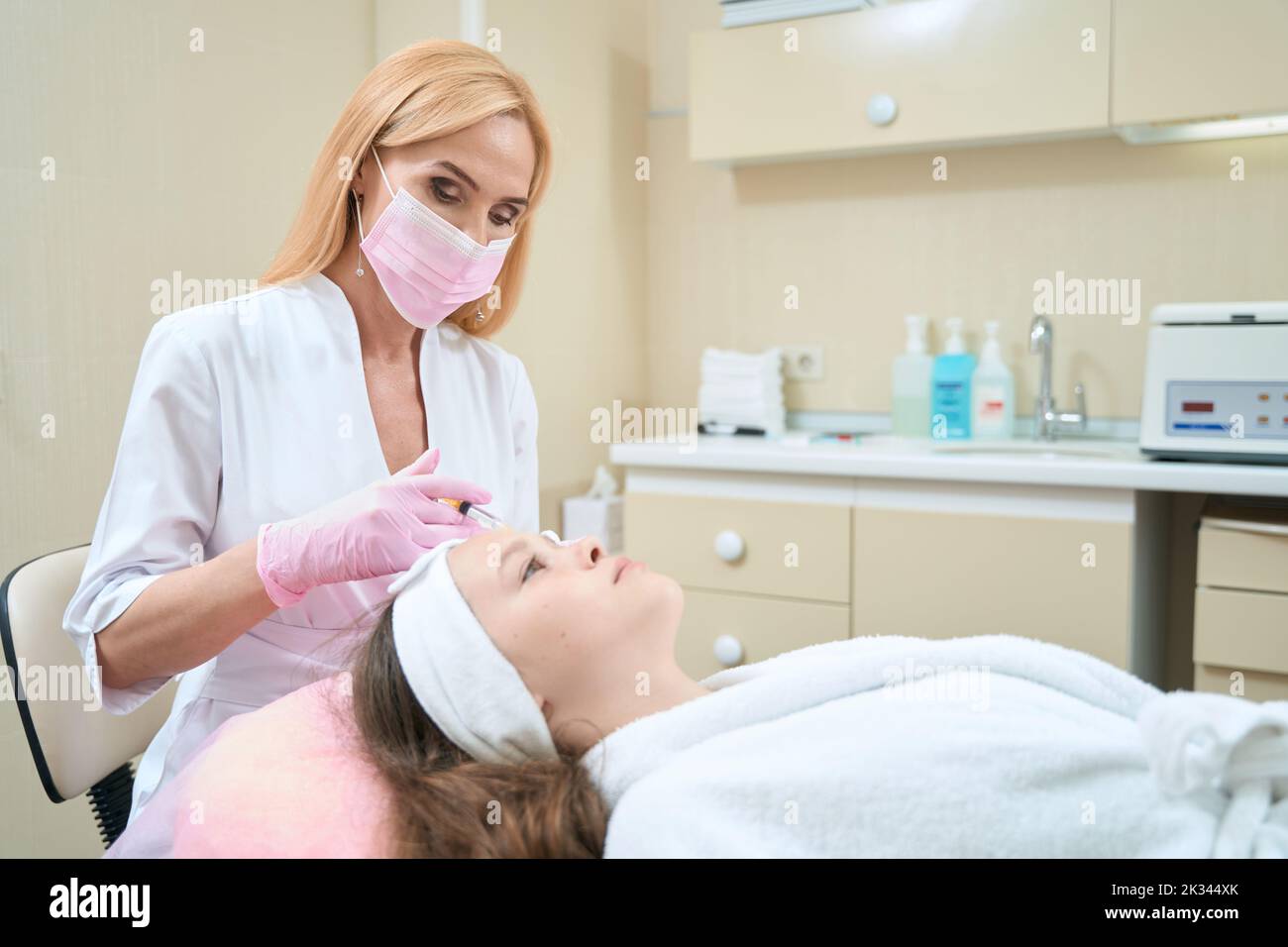 Doctor cosmetologist makes injection in forehead of teenage girl Stock Photo