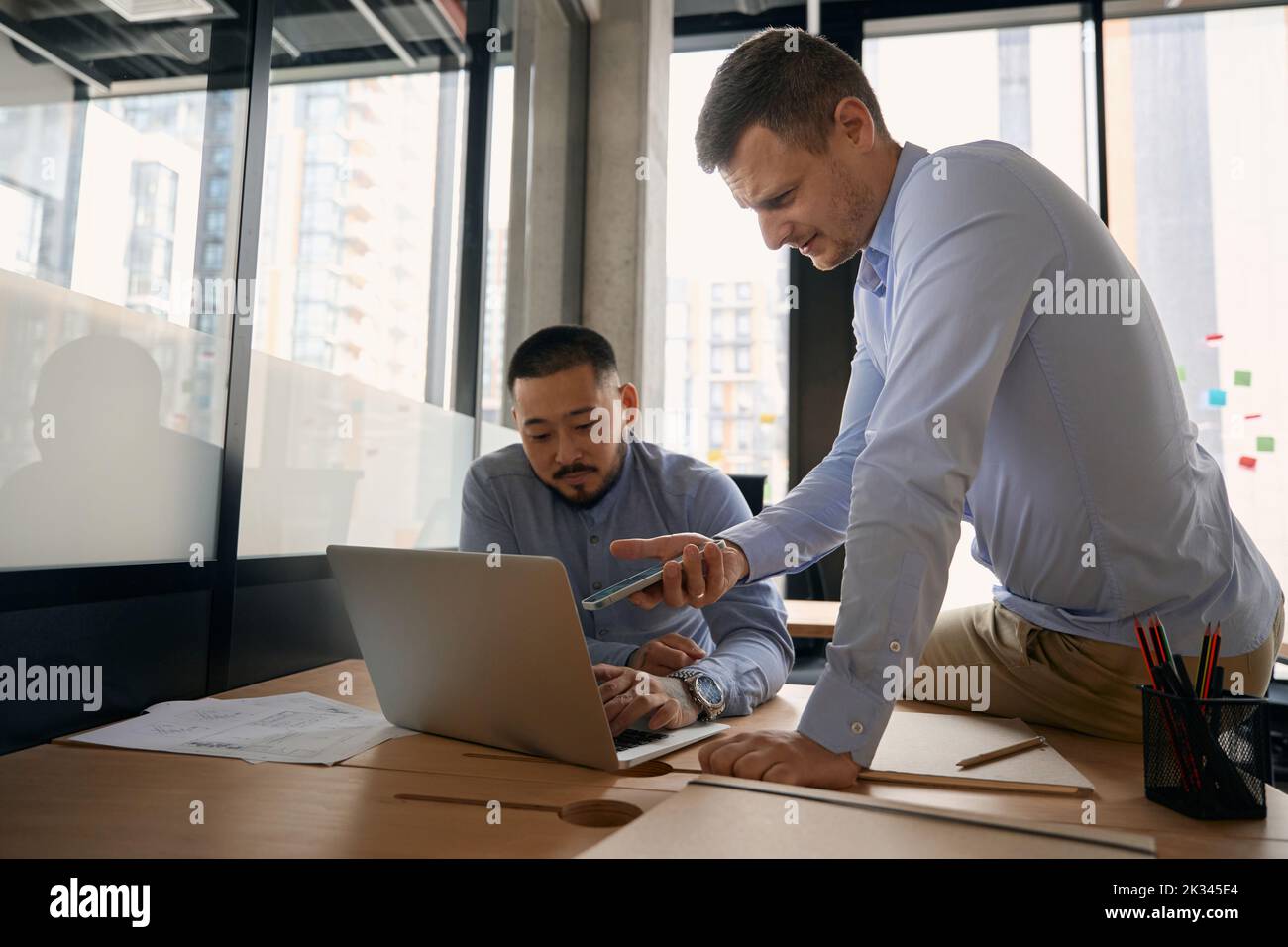 Corporate workers sending files from mobile device to laptop Stock Photo