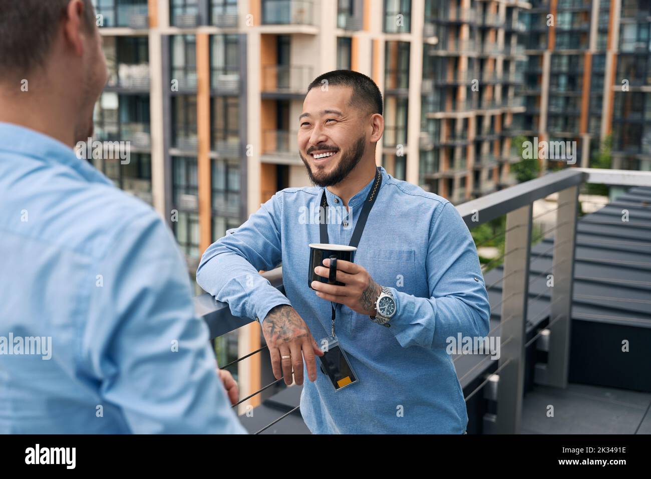 Cheerful corporate worker and his coworker talking on balcony Stock Photo