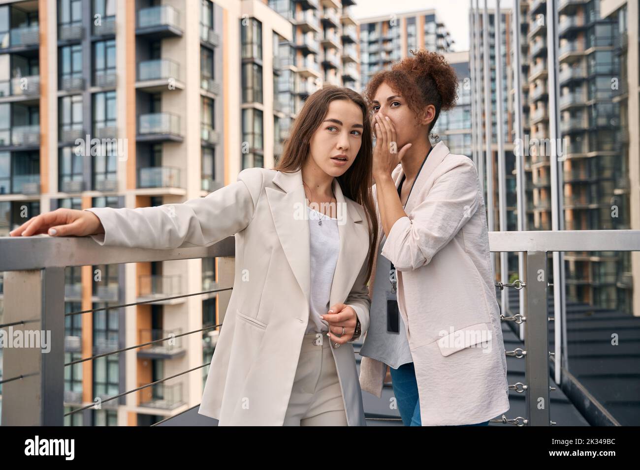 Office employee telling secret to her coworker outdoors Stock Photo
