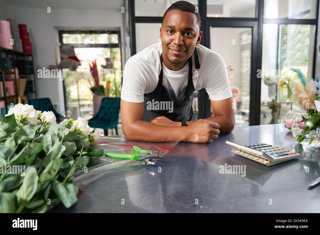 Florist stands in a flower shop and looks at the camera Stock Photo