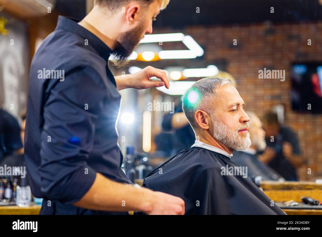 retired man visiting barbershop , sitting in the barber's chair while ...