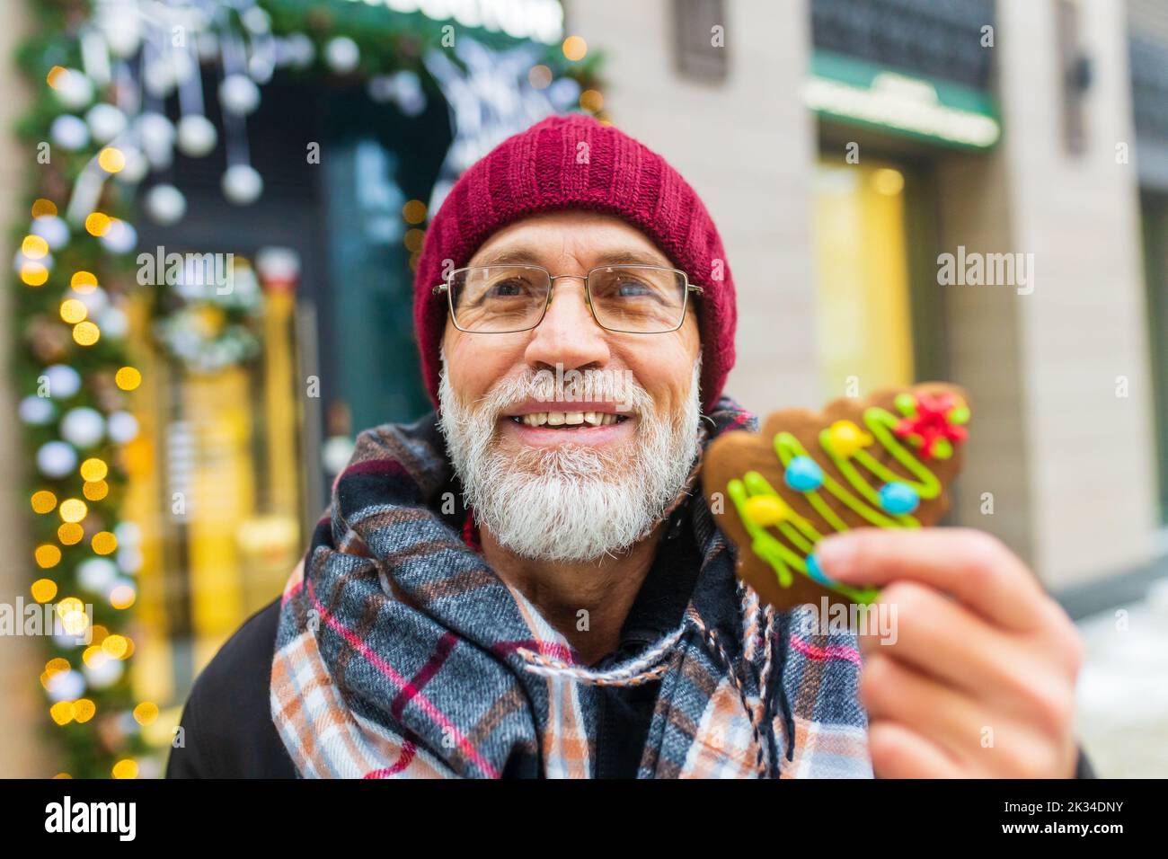 happy man showing green sweet cookie christmas tree shape outdoors in winter market Stock Photo