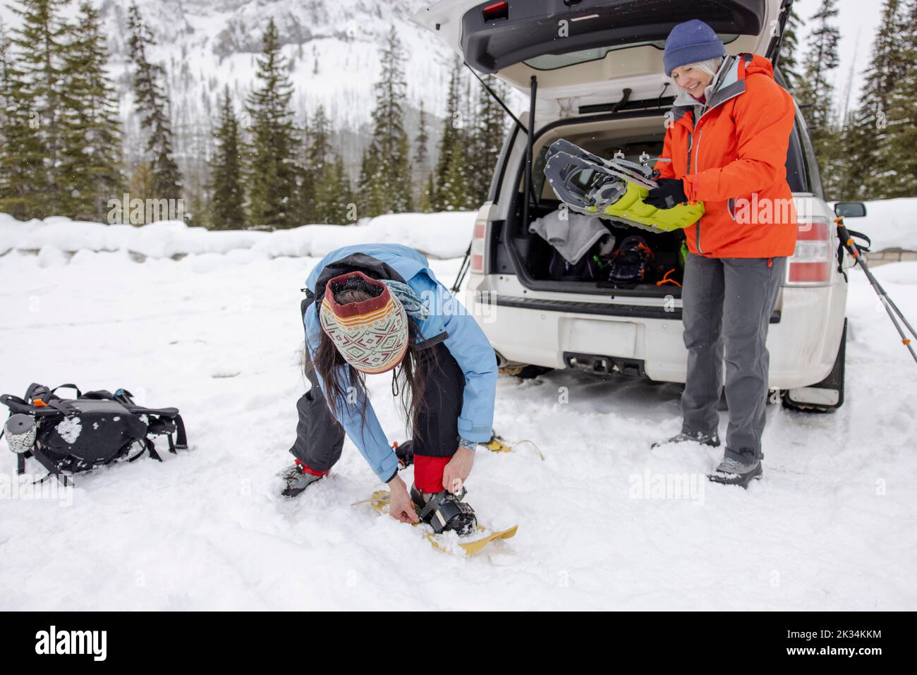 Women putting on snowshoes at back of car in snow Stock Photo