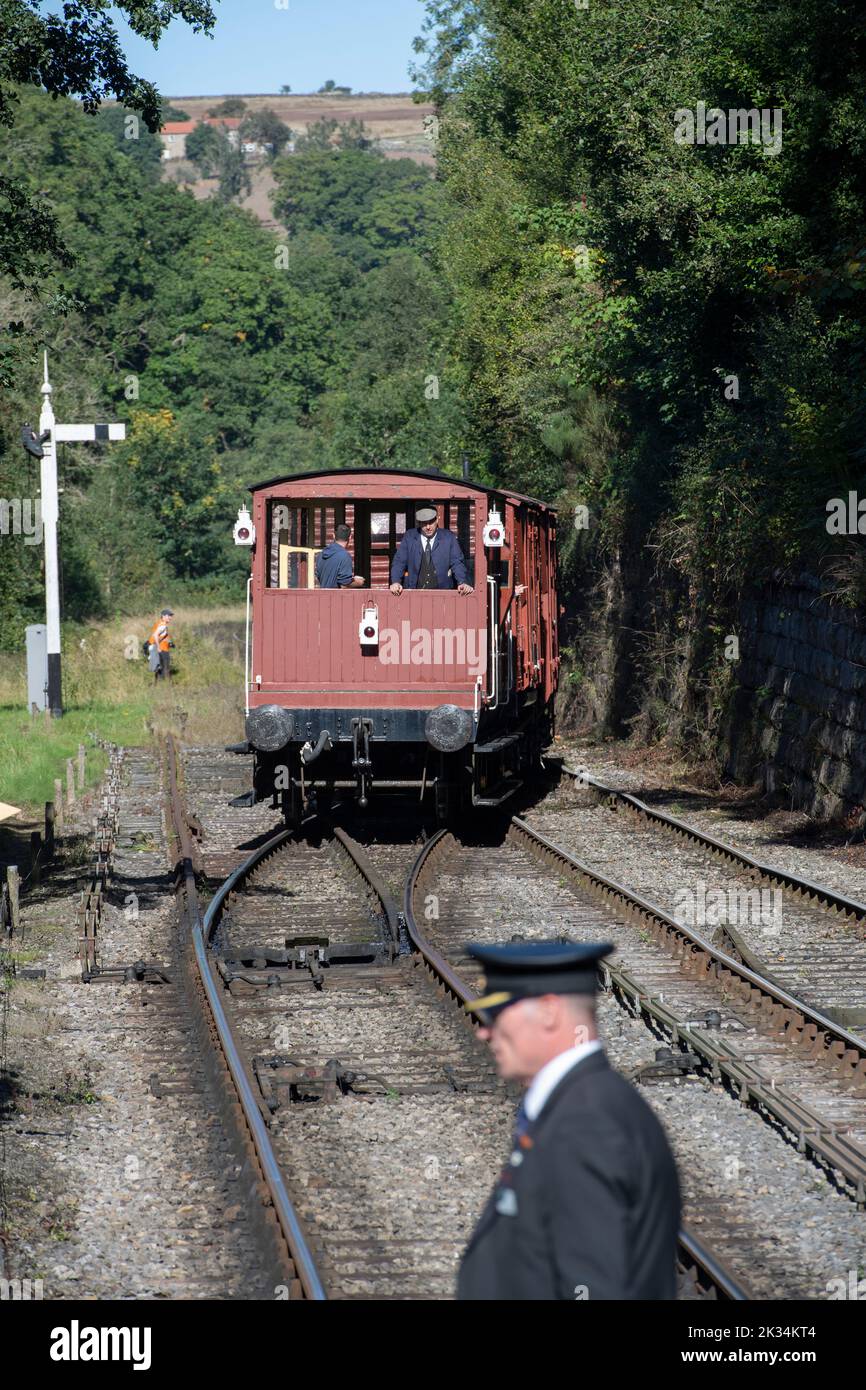 A conductor crossing the track as a steam train leaves Goathland station on the North Yorkshire Moors Railway Stock Photo