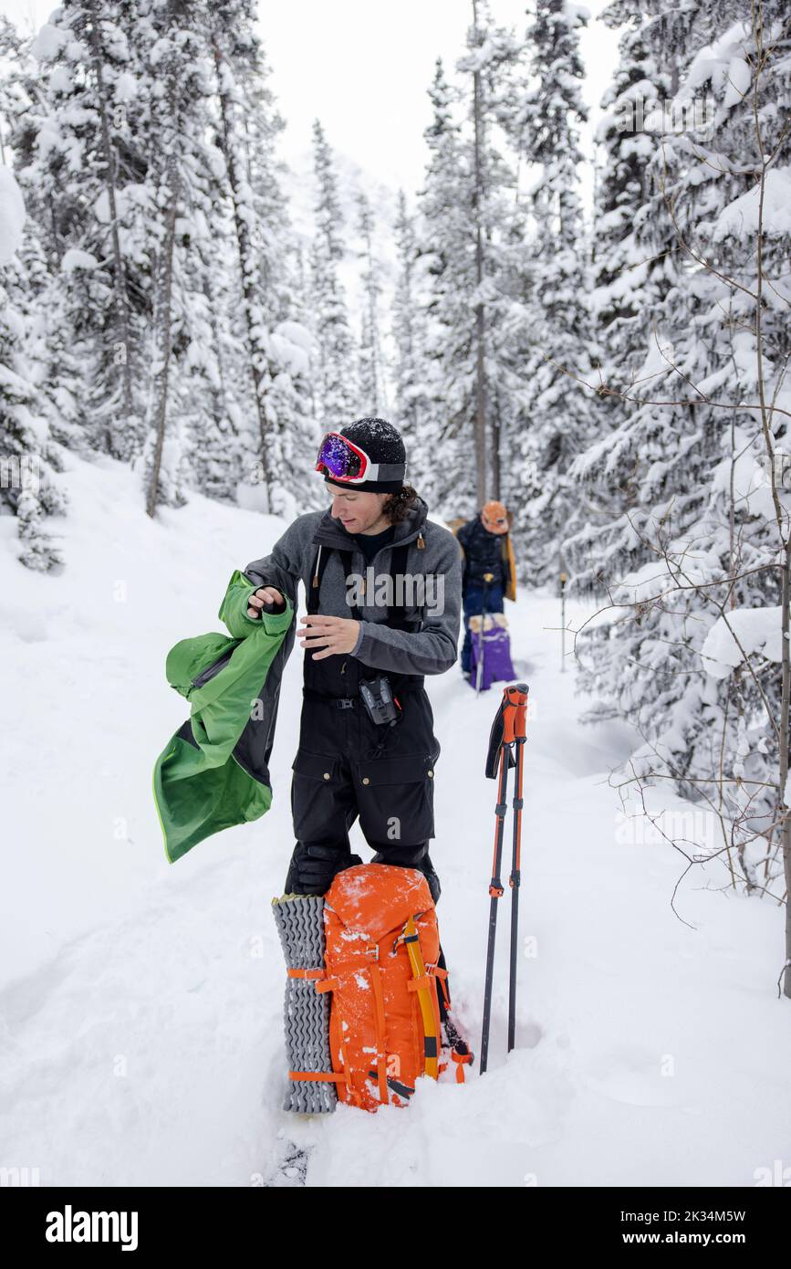 Man removing jacket taking a break from backcountry skiing in snow Stock Photo