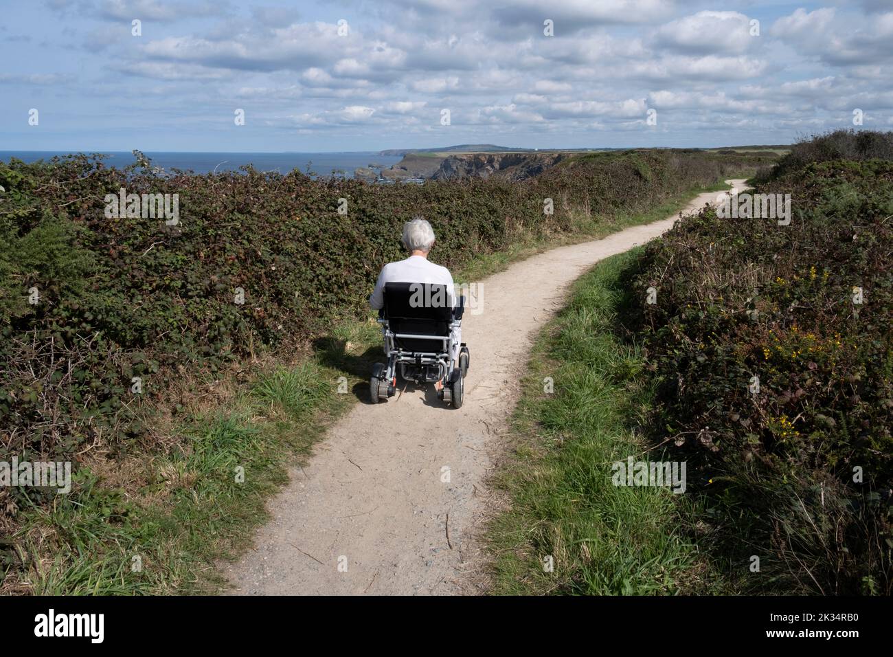 A lady in an electric wheelchair moves along a cliff top coastal path made for wheelchairs in North Cornwall, England. Stock Photo